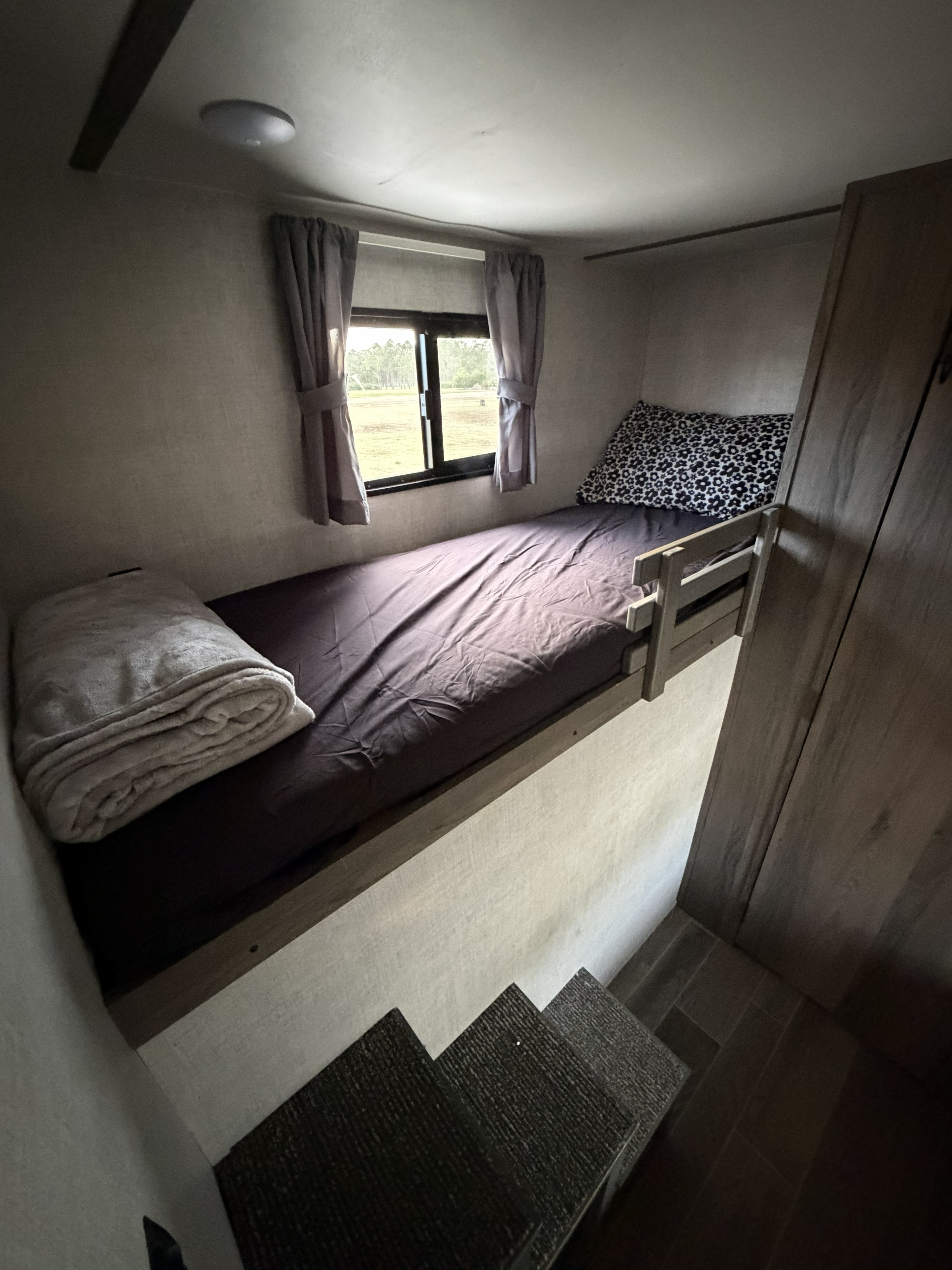 Cozy bunk bed with window and steps in an RV rental. A rolled blanket and patterned pillow add comfort to this compact space.. Gulf Stream Ameri-Lite 2021