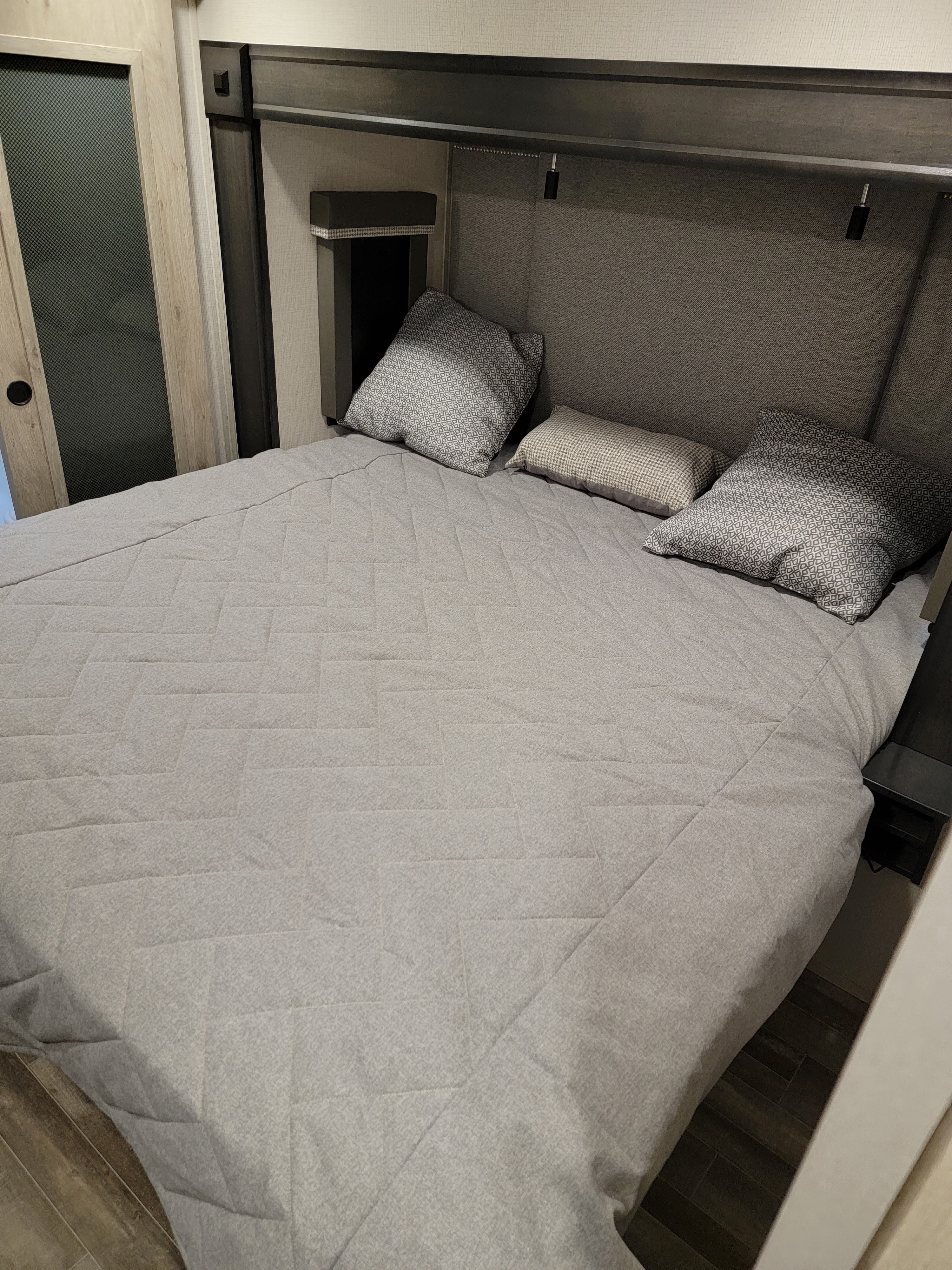 Inviting RV rental bedroom with a gray quilted bed, geometric pillows, built-in headboard lights, and a sliding door.. Keystone RV Alpine 2021