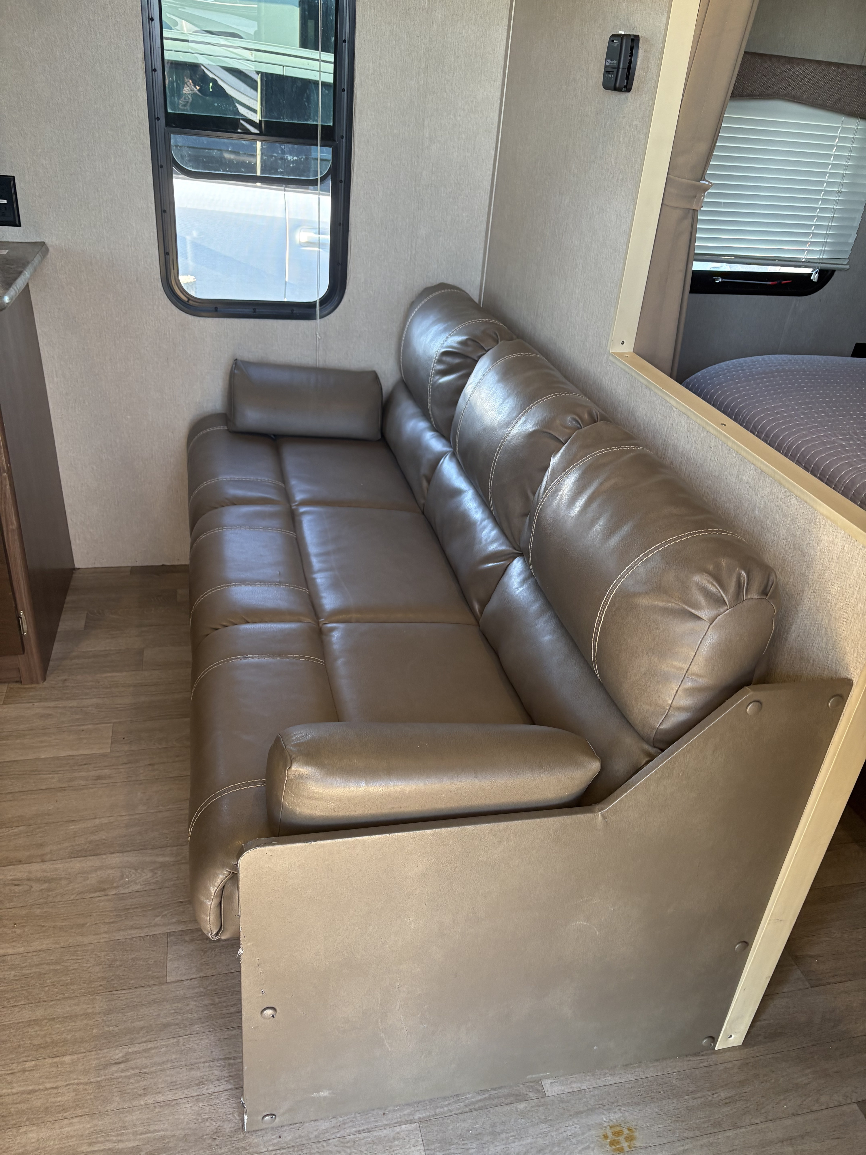 Cozy RV rental interior with a brown faux leather sofa, side window, and glimpse of the sleeping area.. Coleman Lantern 2018