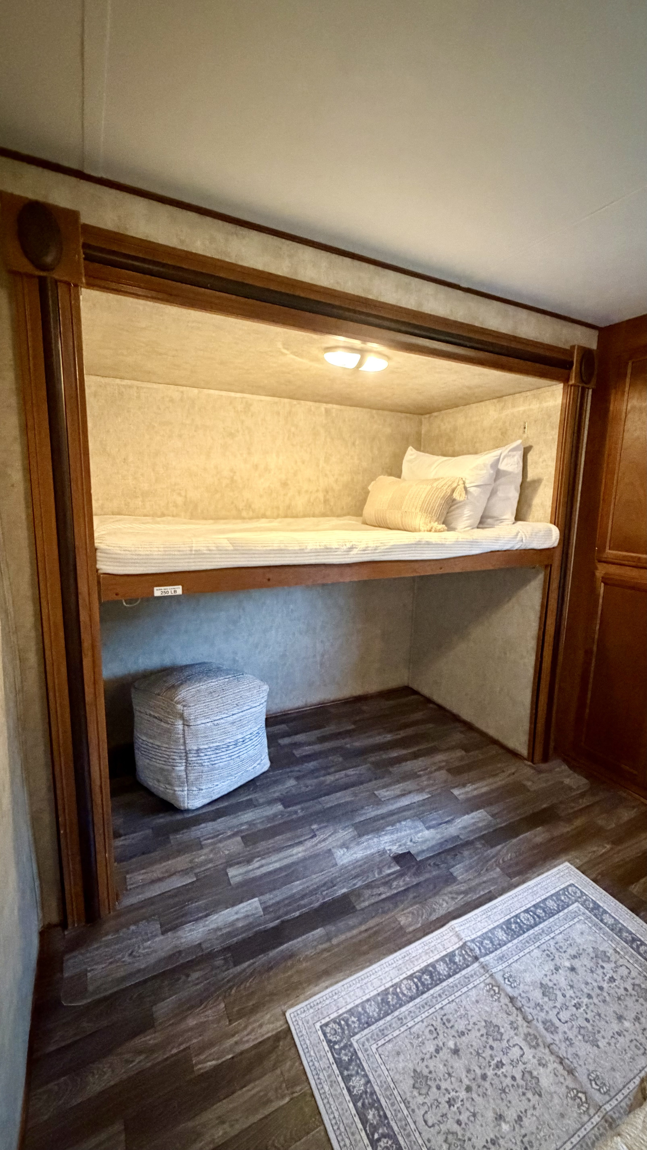 Compact RV rental bunk bed with bedding, pouf, and wood-look flooring. Ideal sleeping area for travel.. Avenger Avenger Trailer 2015