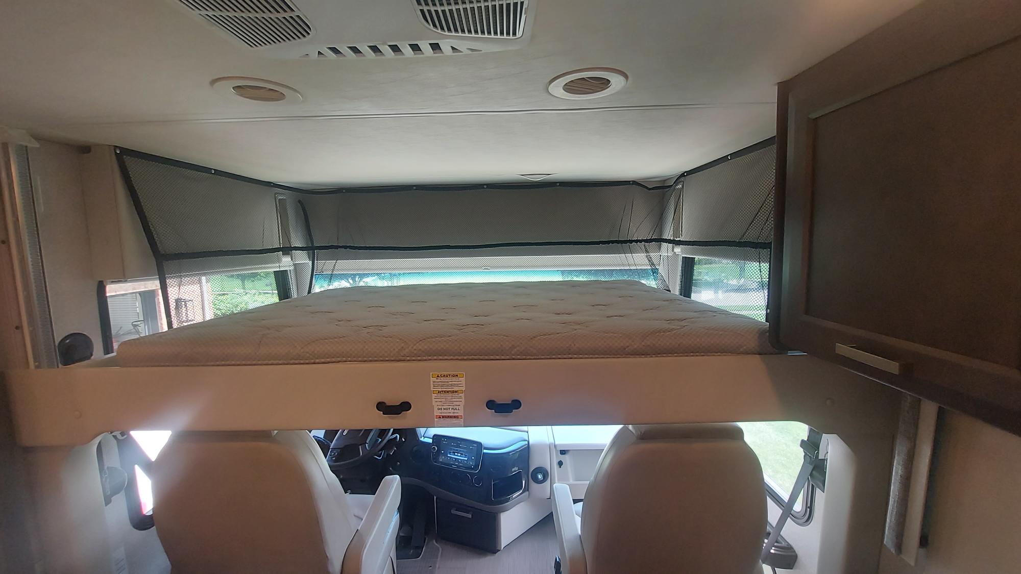 This RV rental interior features an overhead bunk bed with safety netting, situated above the driver's and passenger's seats.. Thor Palazzo 2023