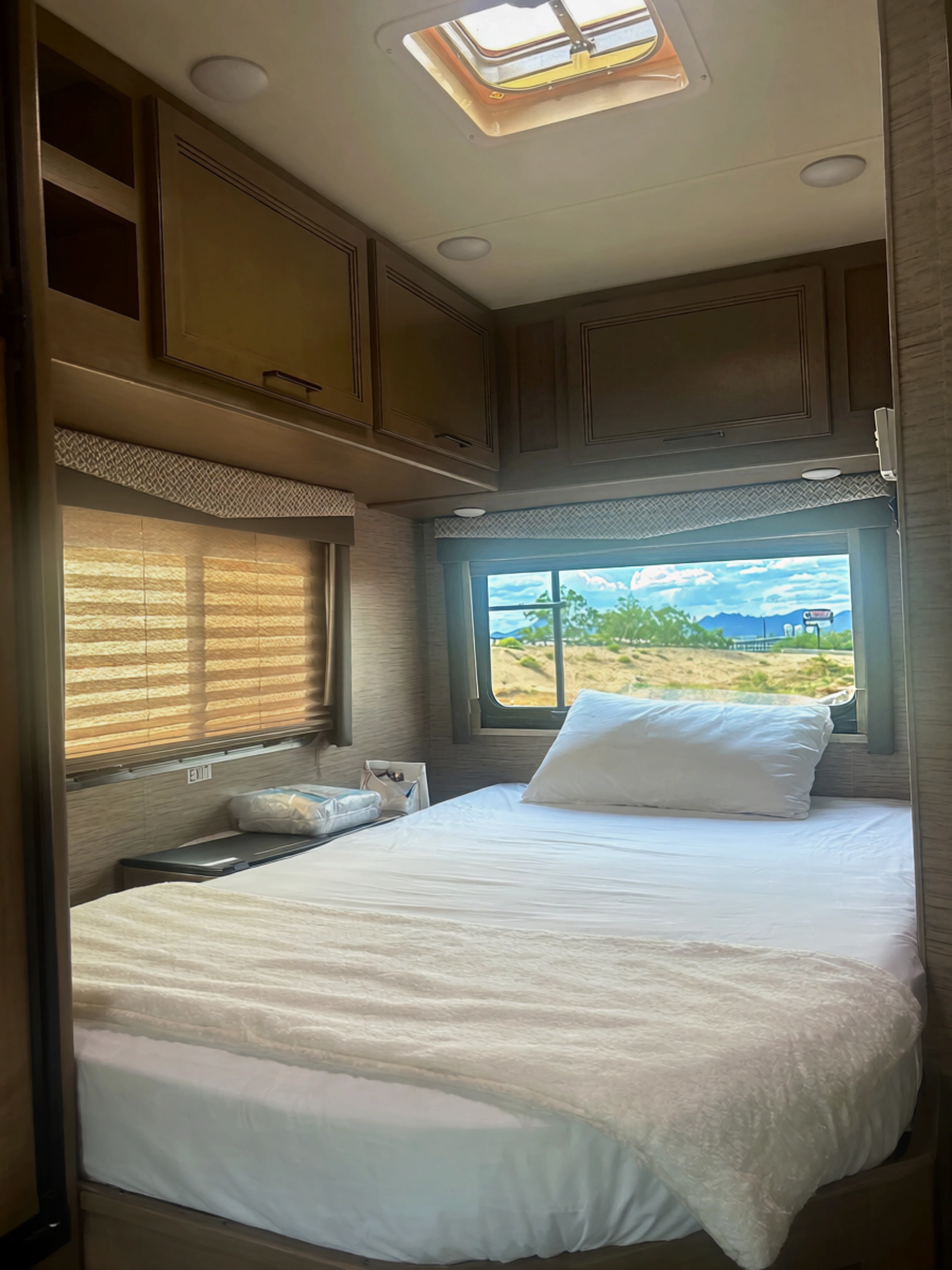 Inside this RV rental: a bright sleeping area with a bed, scenic window overlooking the desert, and practical overhead storage.. Thor Four Winds 2021