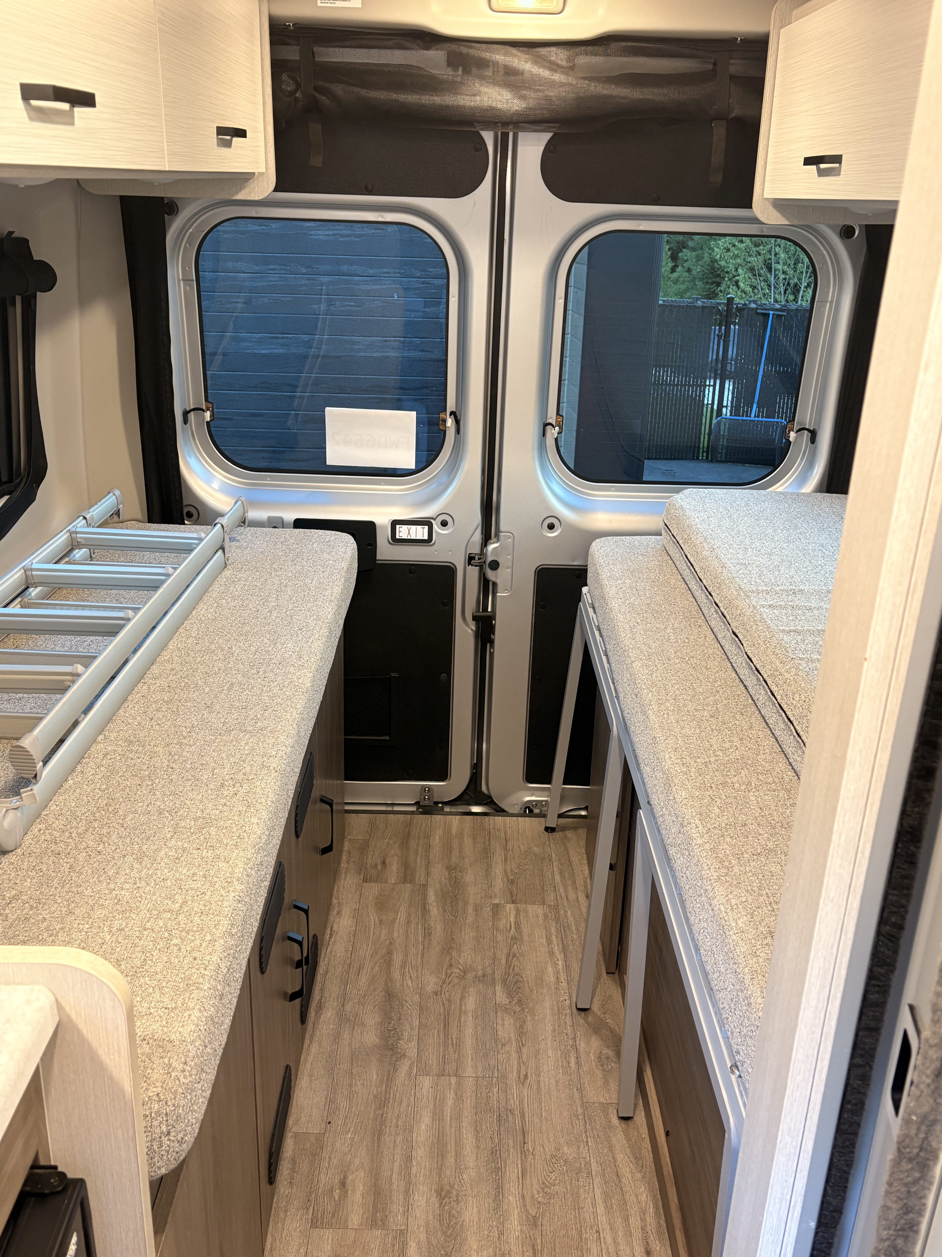 This rv rental camper van interior features two bunk beds, a ladder, wood flooring, and rear windows, ready for travel.. Thor Twist 2025