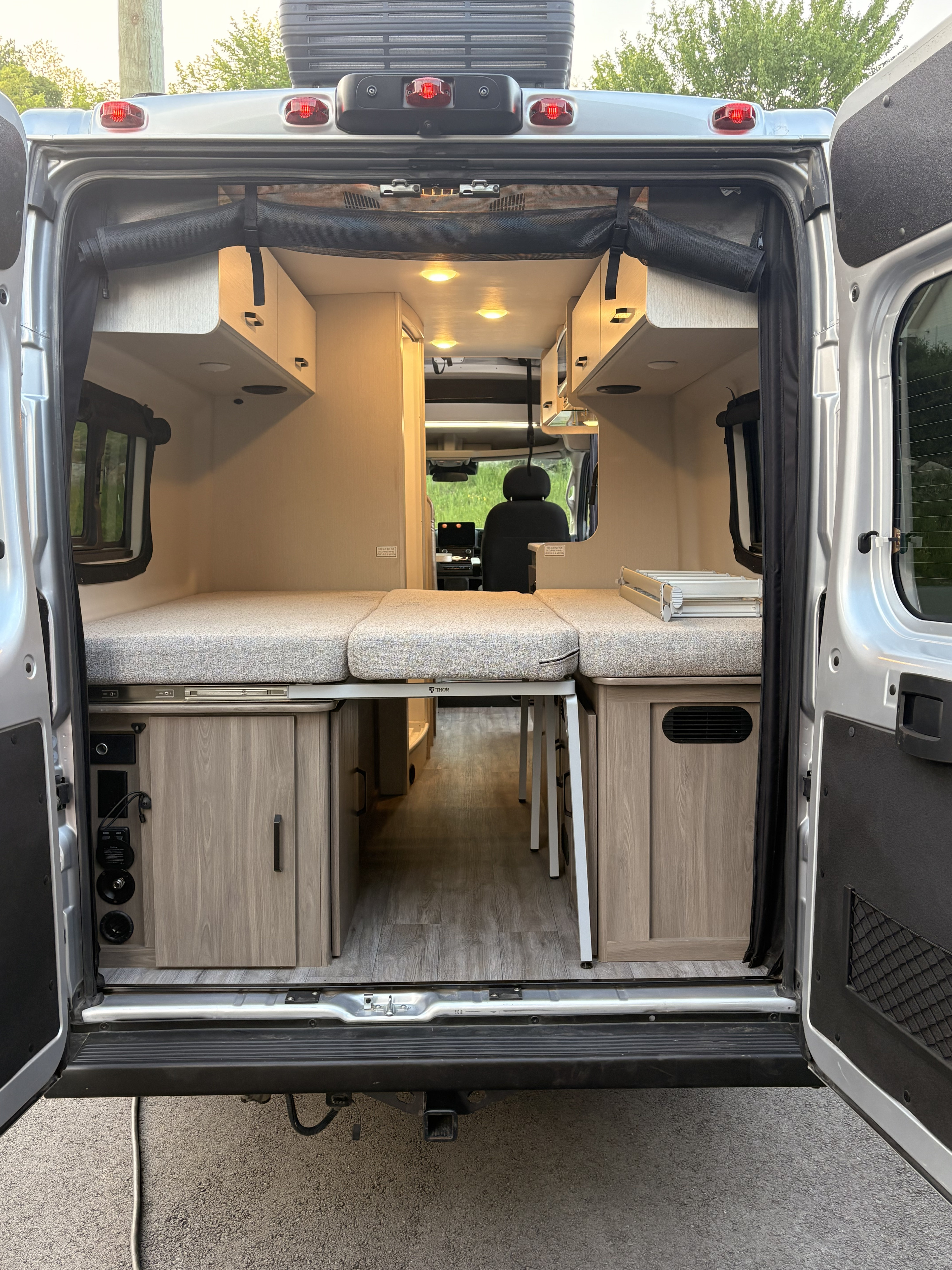 Inside an rv rental: rear doors open to reveal a convertible bed, under-bed storage, and controls. Ready for travel.. Thor Twist 2025