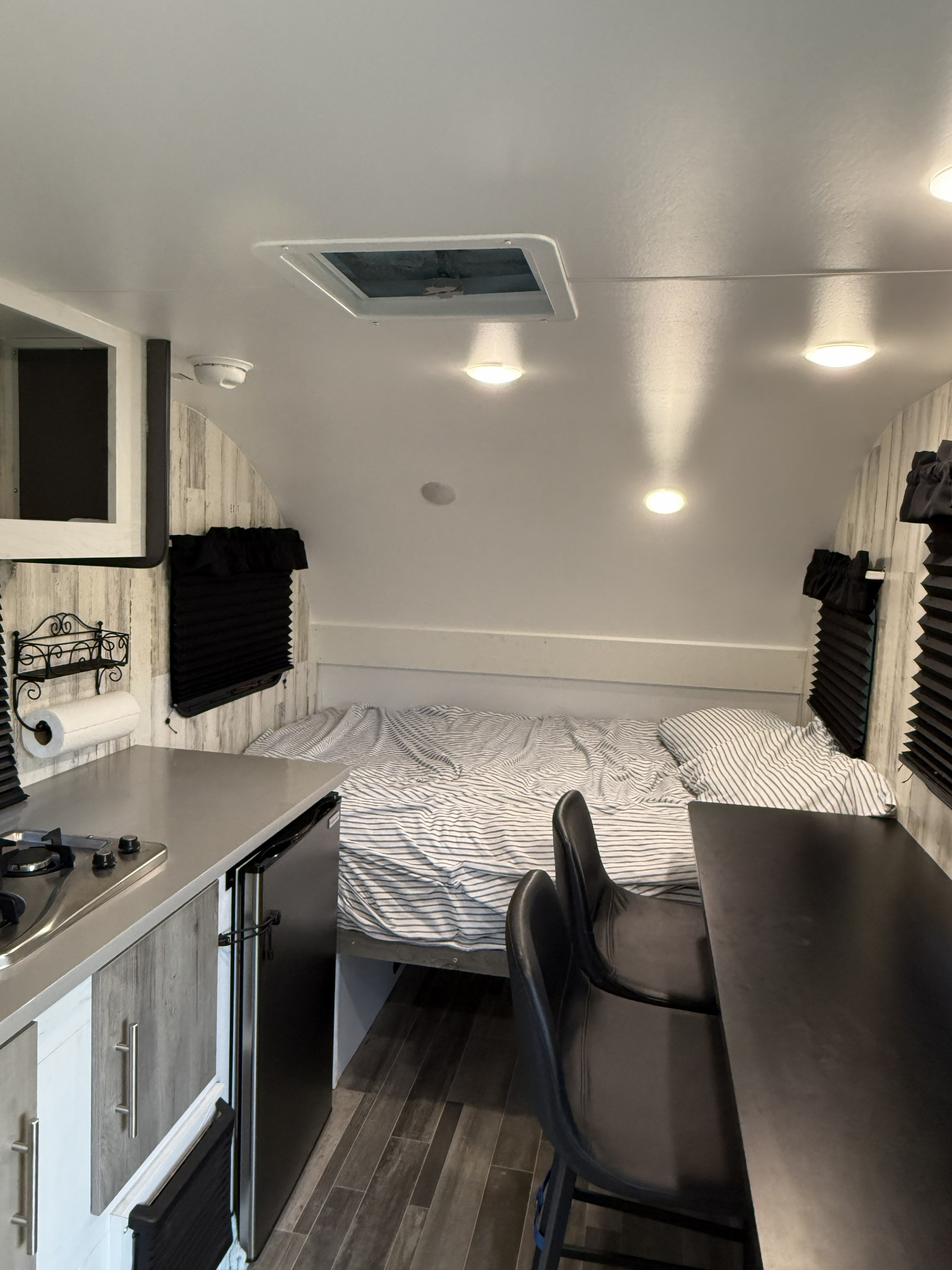 Cozy RV rental interior with a compact kitchen, bed with striped bedding, and a small dining area. Perfect for travel.. Travel Lit Rove Lite 55Mtm 14FS 2025