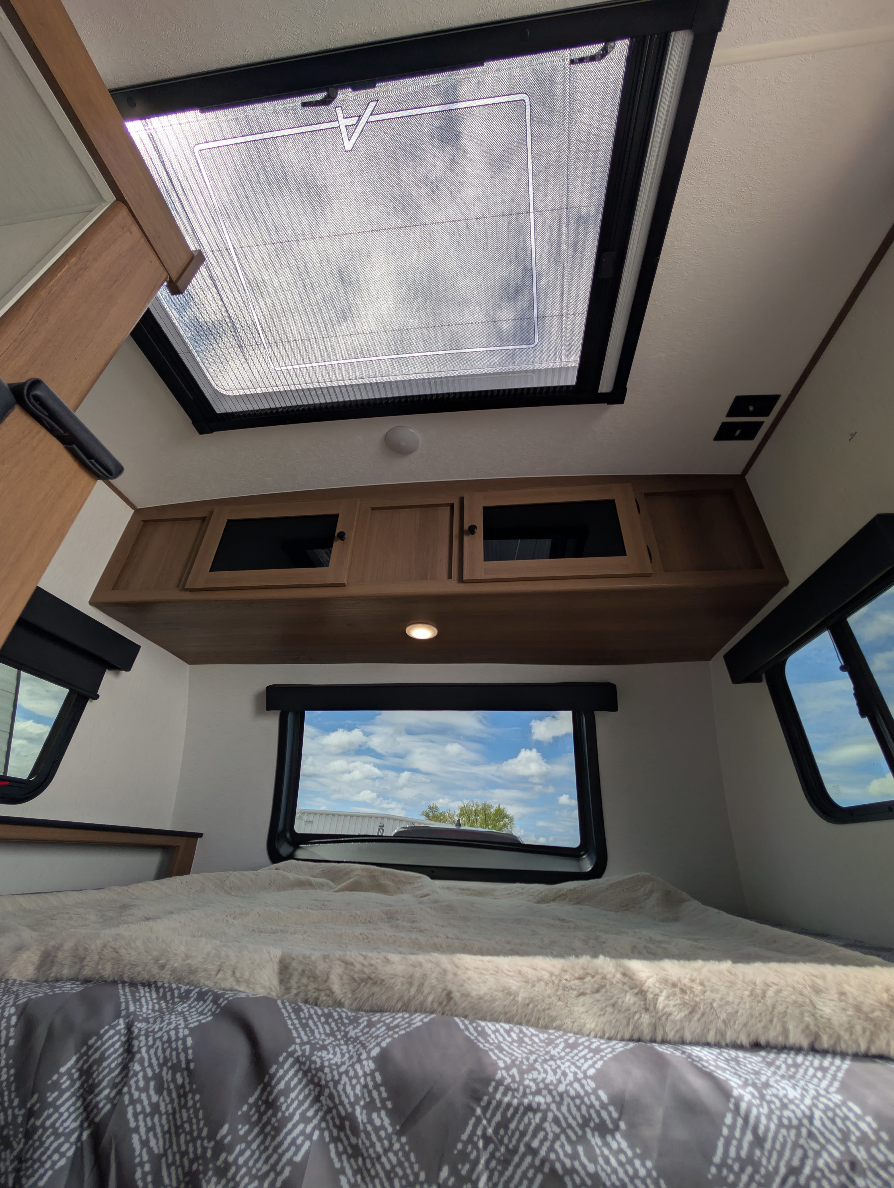 Cozy RV rental bedroom with a skylight and windows showing the sky, overhead cabinets, and a fluffy blanket on the bed.. Forest River Apex Nano 194 BHS 2026