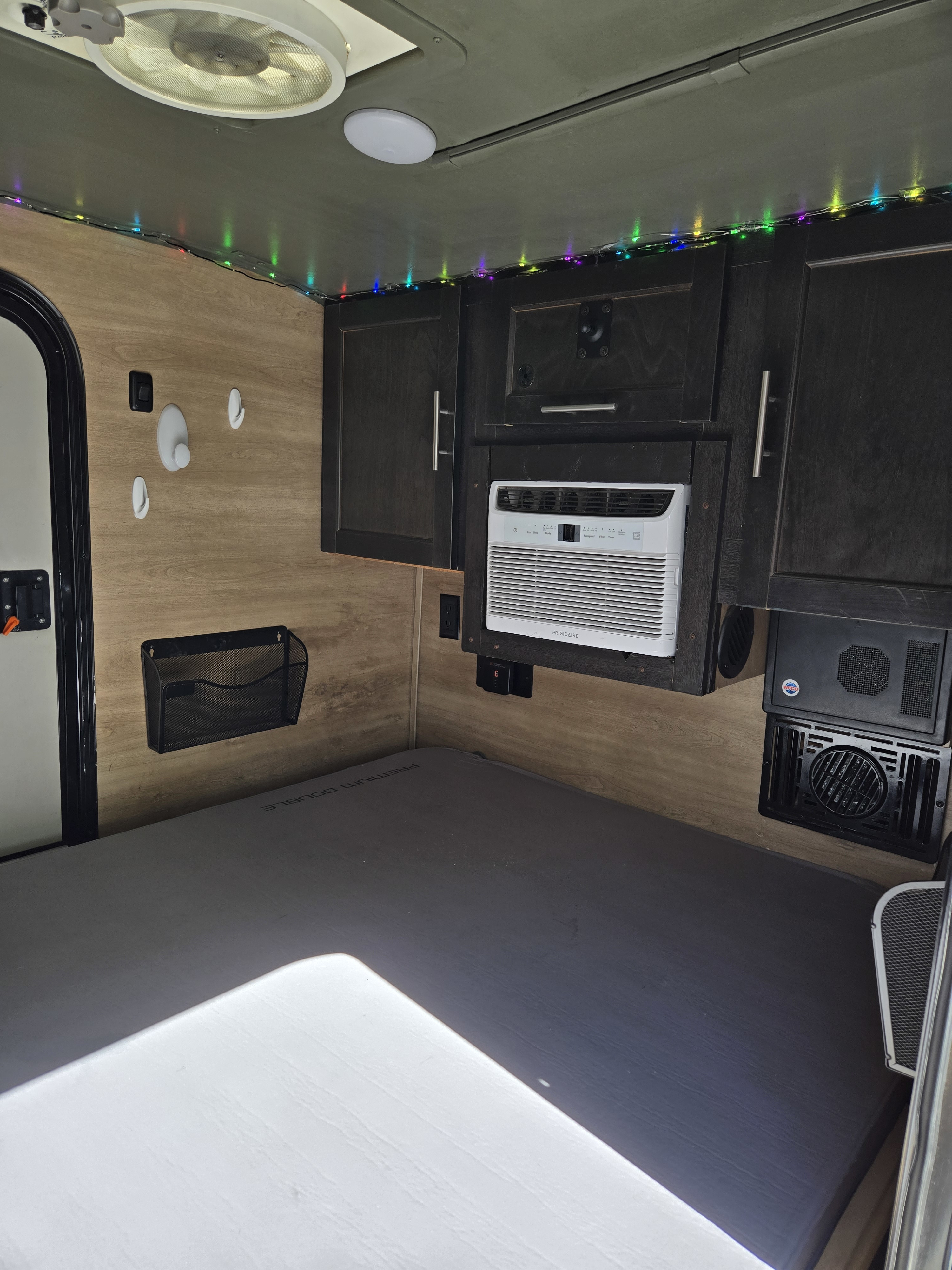 Inside a comfortable rv rental: a bed, Frigidaire AC, dark cabinets, ceiling fan, and string lights create a functional space.. Braxton Creek Bushwhacker 2021