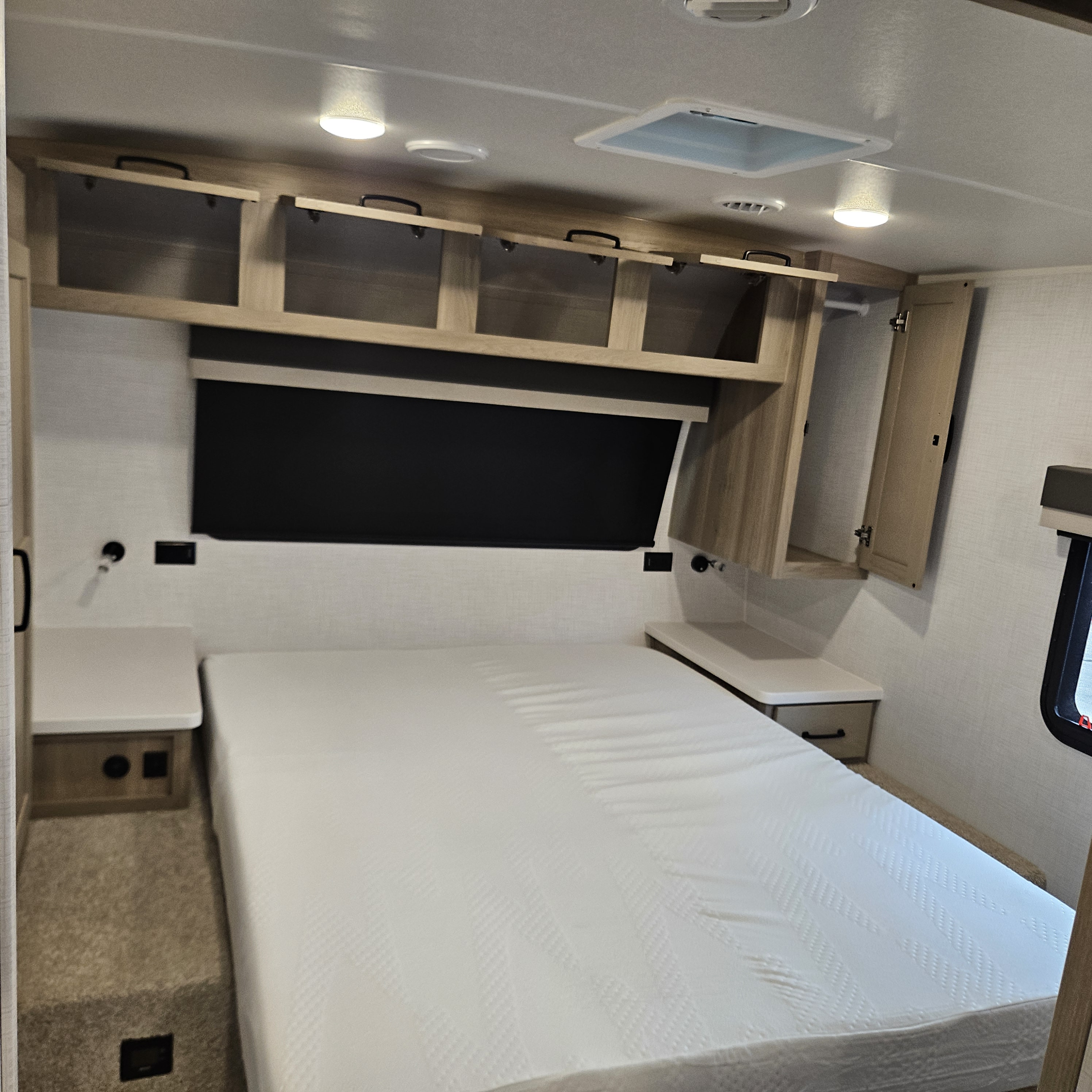 Inside an RV rental bedroom: a comfortable bed with overhead storage cabinets, nightstands, and a wardrobe.. Forest River Flagstaff Micro Lite 2025