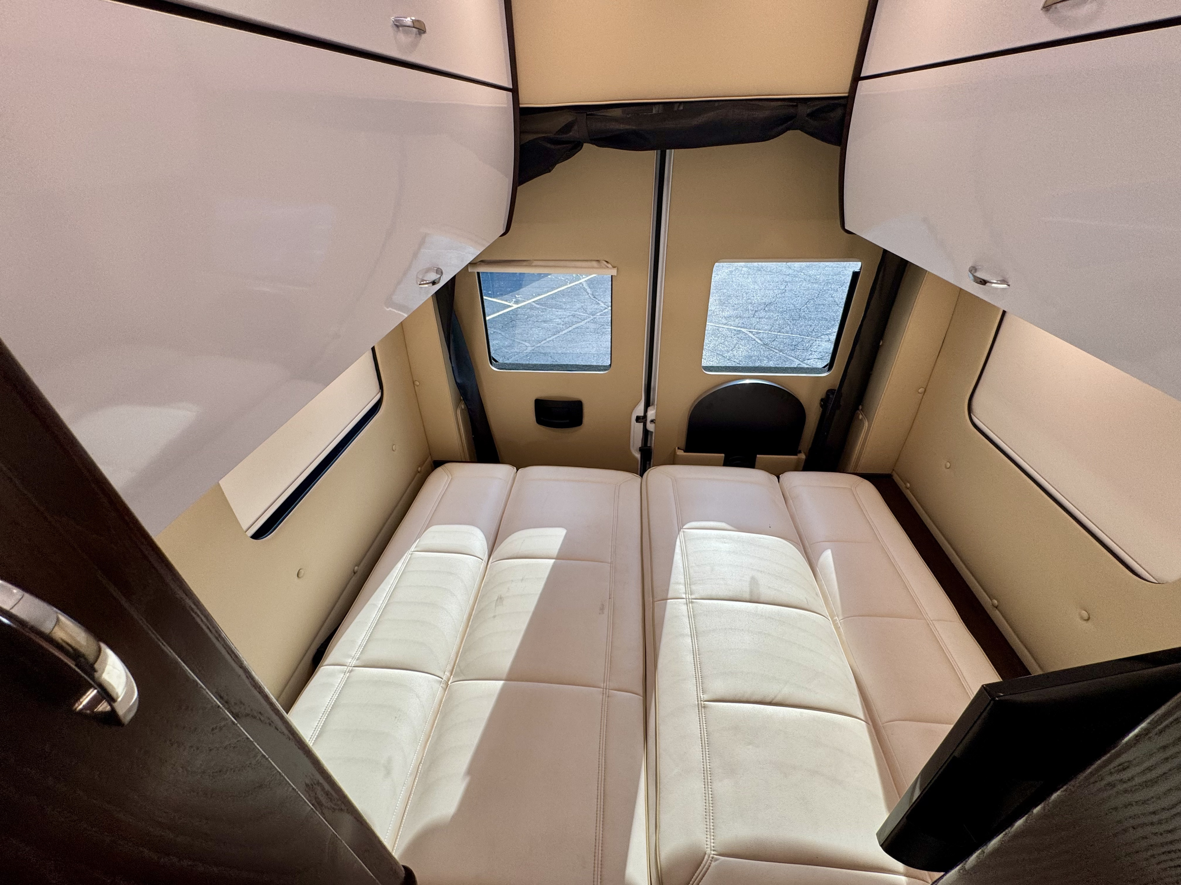 Inside this spacious RV rental: two plush beige sleeping/lounge benches, overhead cabinets, and rear windows for light.. REGC National 2019