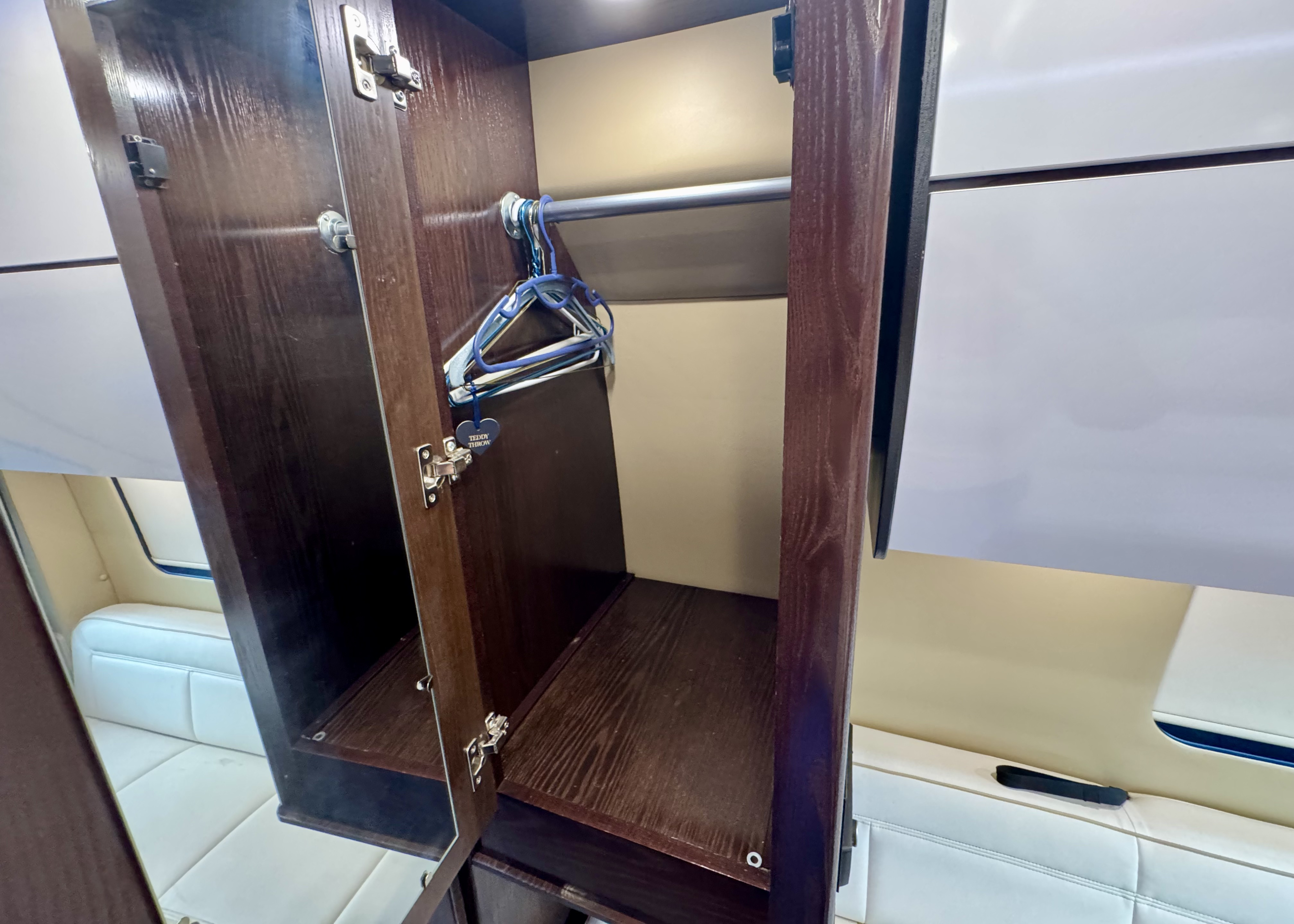 This RV rental features an open wooden closet with a hanging rod, blue hangers, and a shelf. A "Teddy Throw" tag is visible.. REGC National 2019
