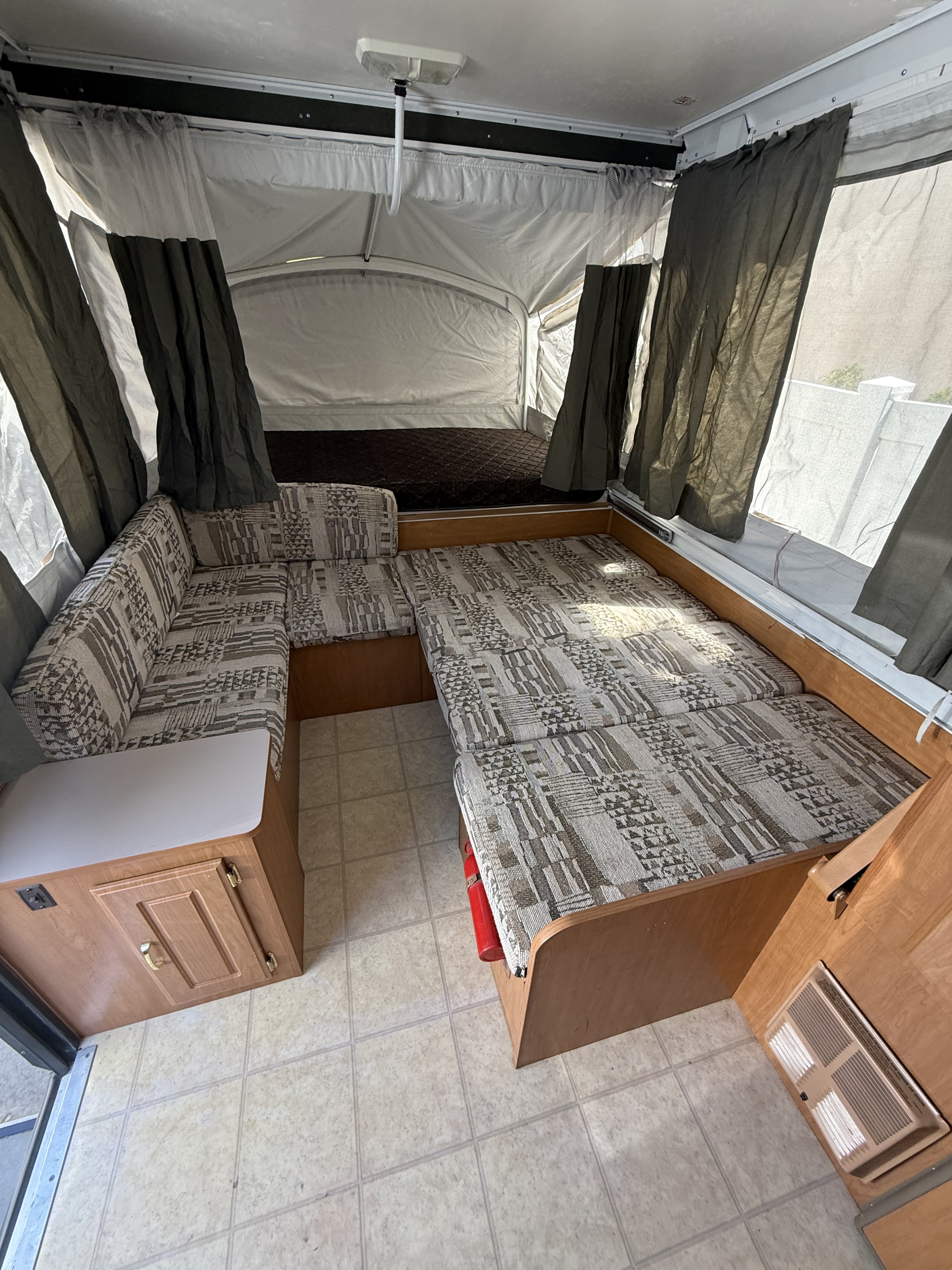 This RV rental offers a pop-up camper interior featuring a convertible dinette bed, additional bunk, and practical tiled floor.. Coleman Grand Tour 2003