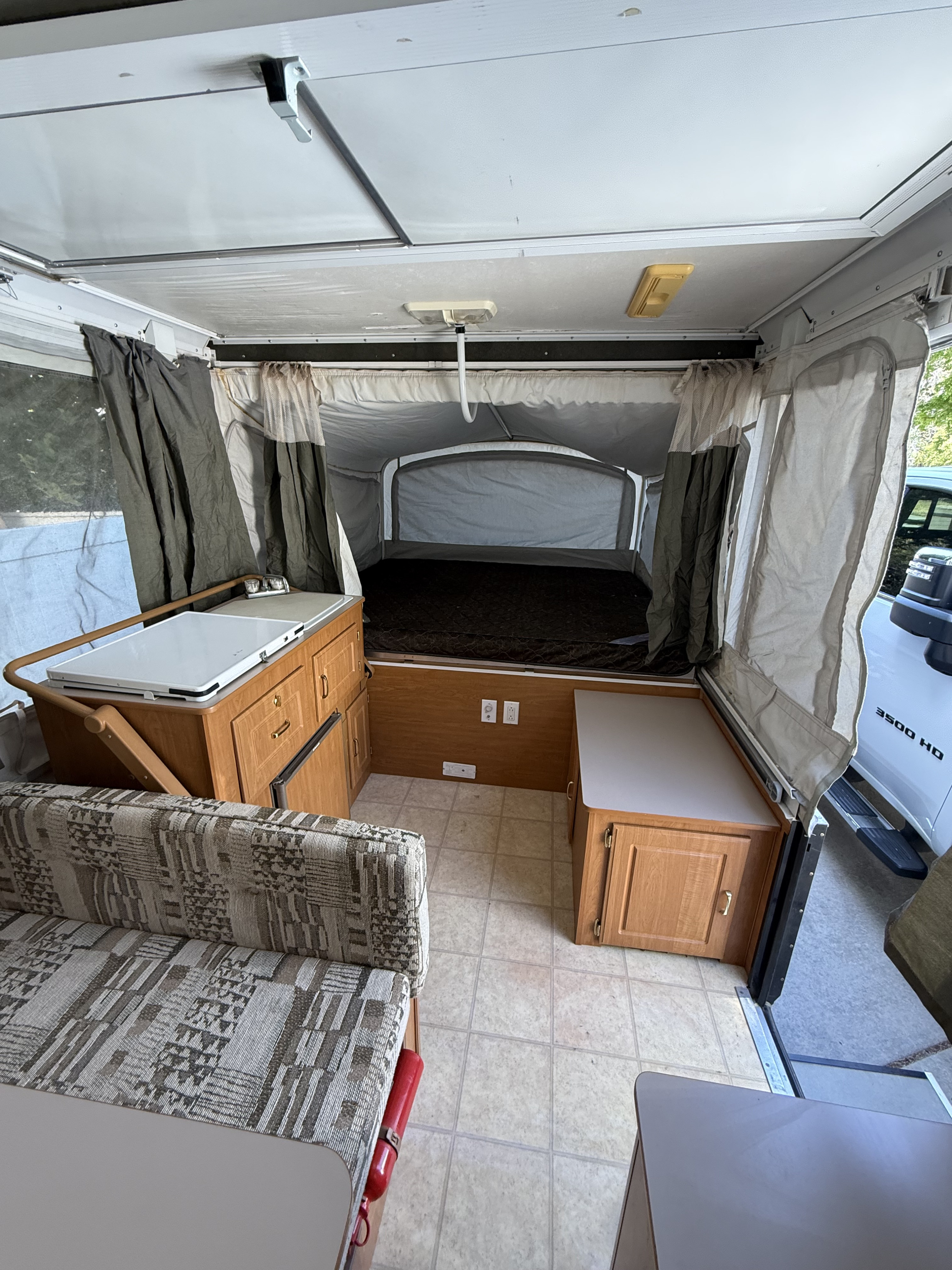 Interior of a pop-up camper RV rental with a bed, small kitchen, and dinette, showing the functional layout.. Coleman Grand Tour 2003