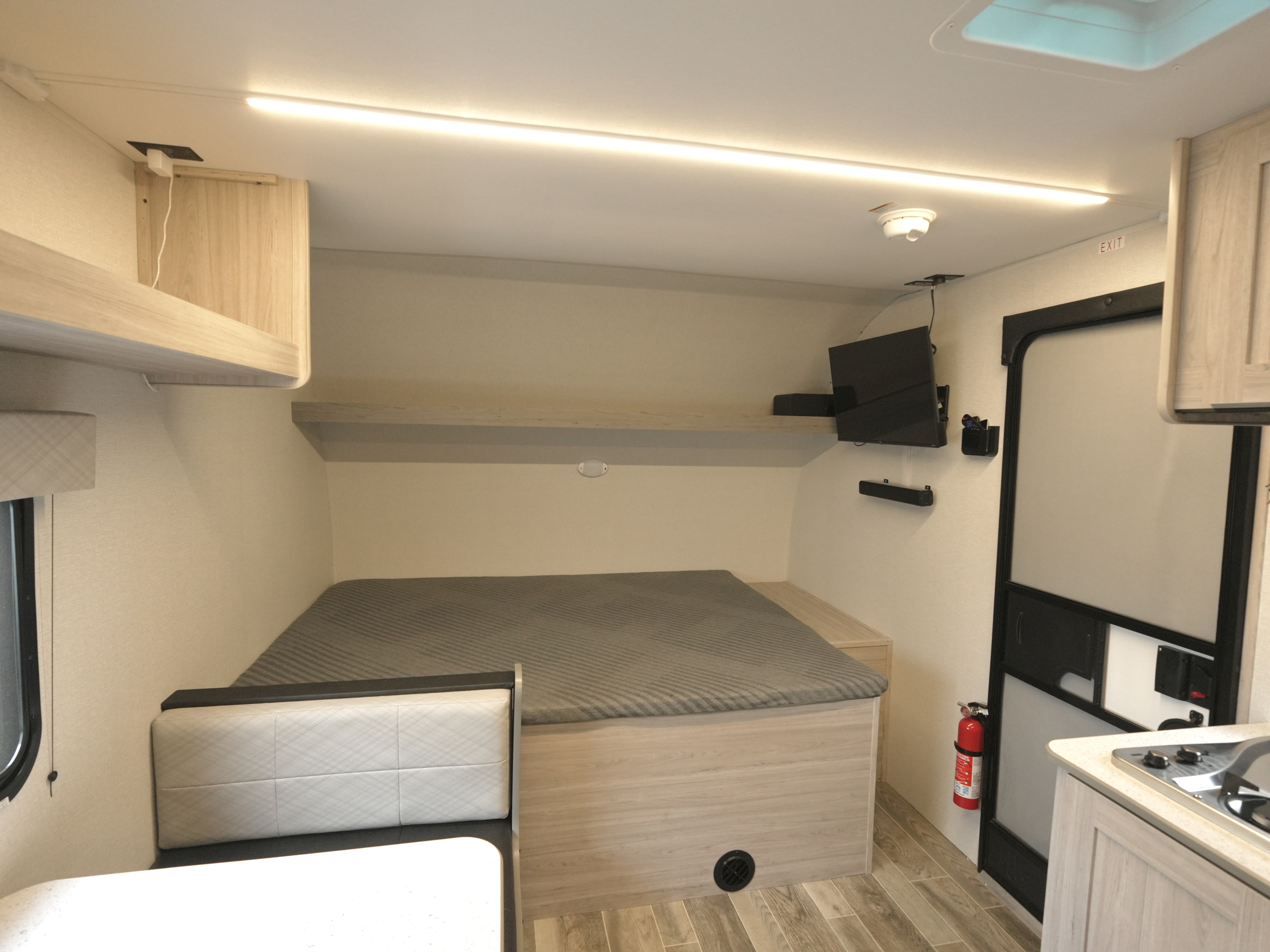 Compact RV rental interior with a cozy bed, dinette, overhead storage, TV, and small kitchen area for efficient travel.. Heartland RVs Mallard 2025