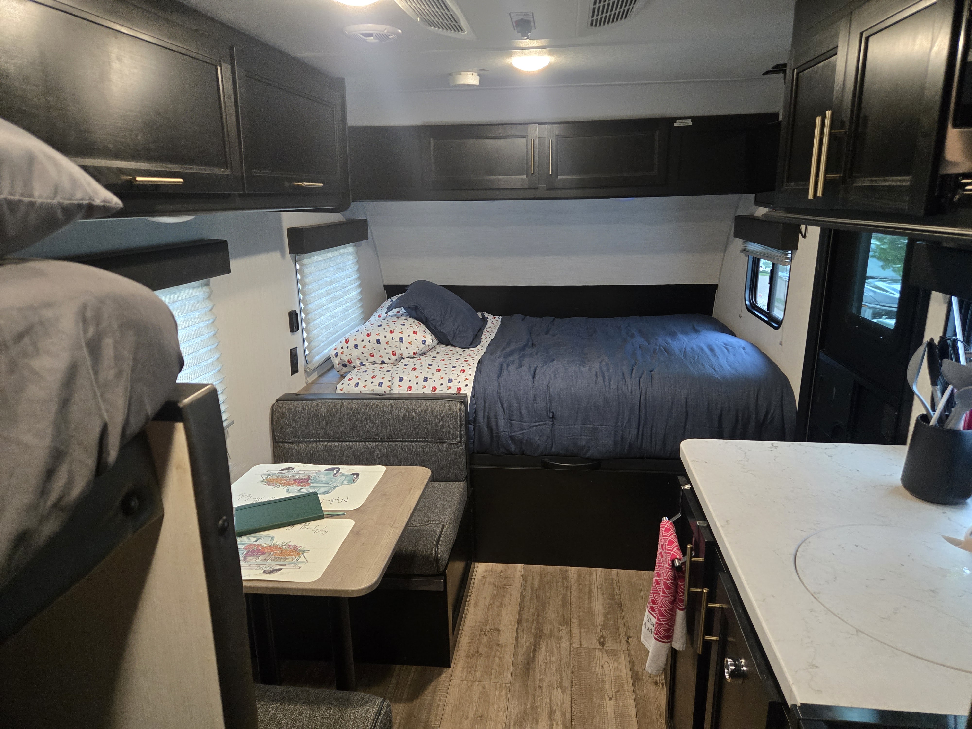 Cozy RV rental interior: bed, dining booth, kitchen counter, dark cabinets. Compact living with bunk bed partially visible.. Forest River Cherokee Wolf Pup 2022