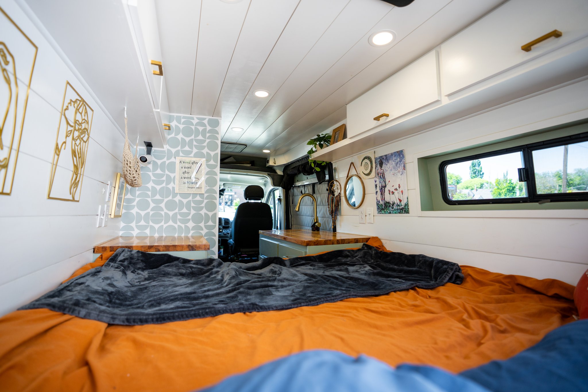 Discover this modern RV rental's interior: a comfortable bed, compact kitchen with gold accents, and bright, inviting decor.. Dodge Ram Promaster 2500 2022