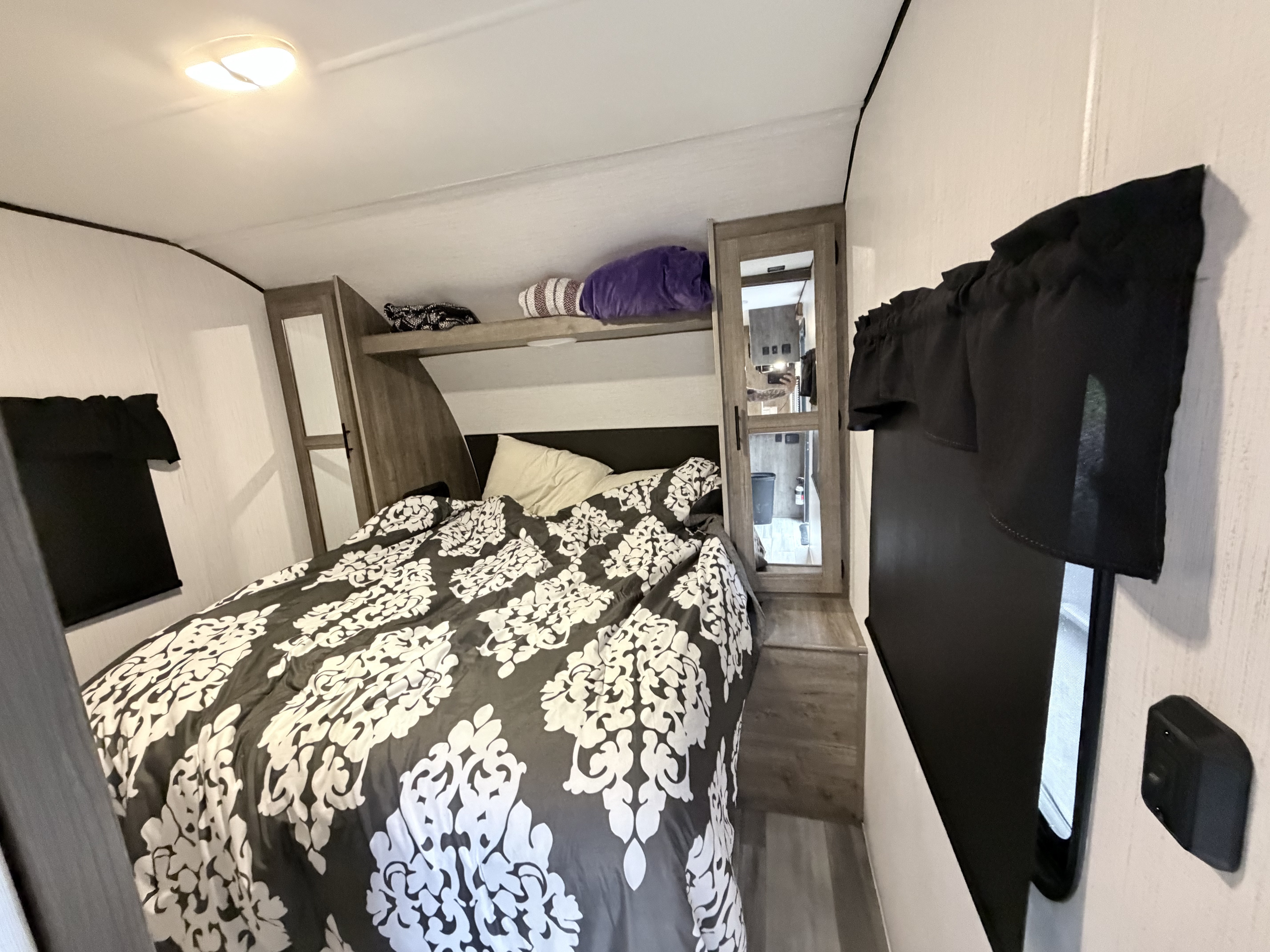 Cozy RV rental bedroom with a dark and white patterned bedspread, practical overhead storage, and bright lighting.. Heartland RVs Pioneer 2021