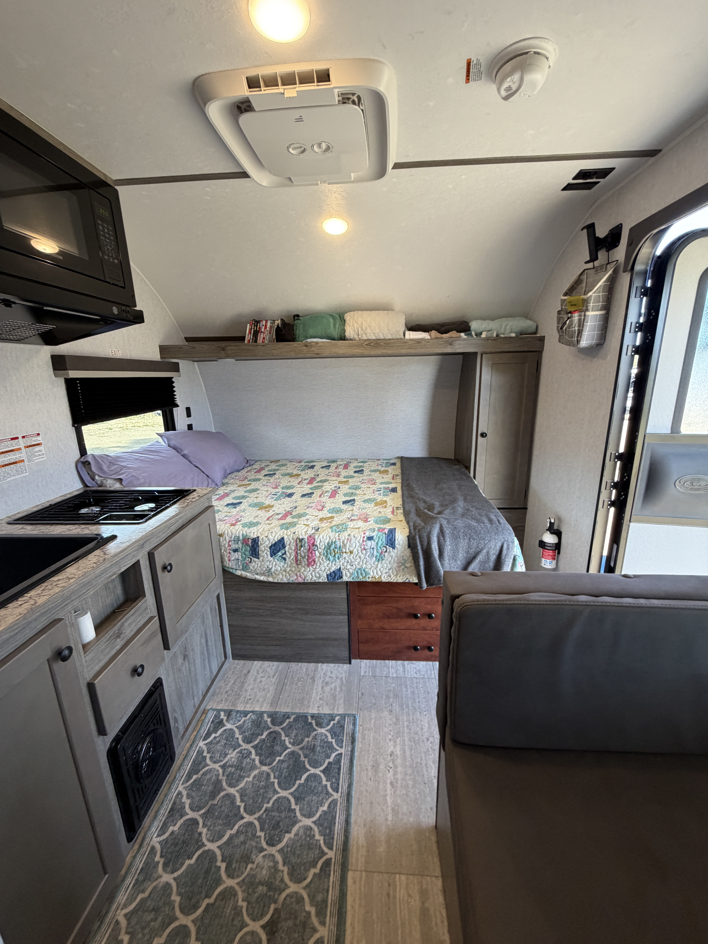 RV rental interior: a comfy bed with colorful quilt, kitchenette, dinette, and overhead storage optimize this compact space.. Sunset Park RV SunRay 2025