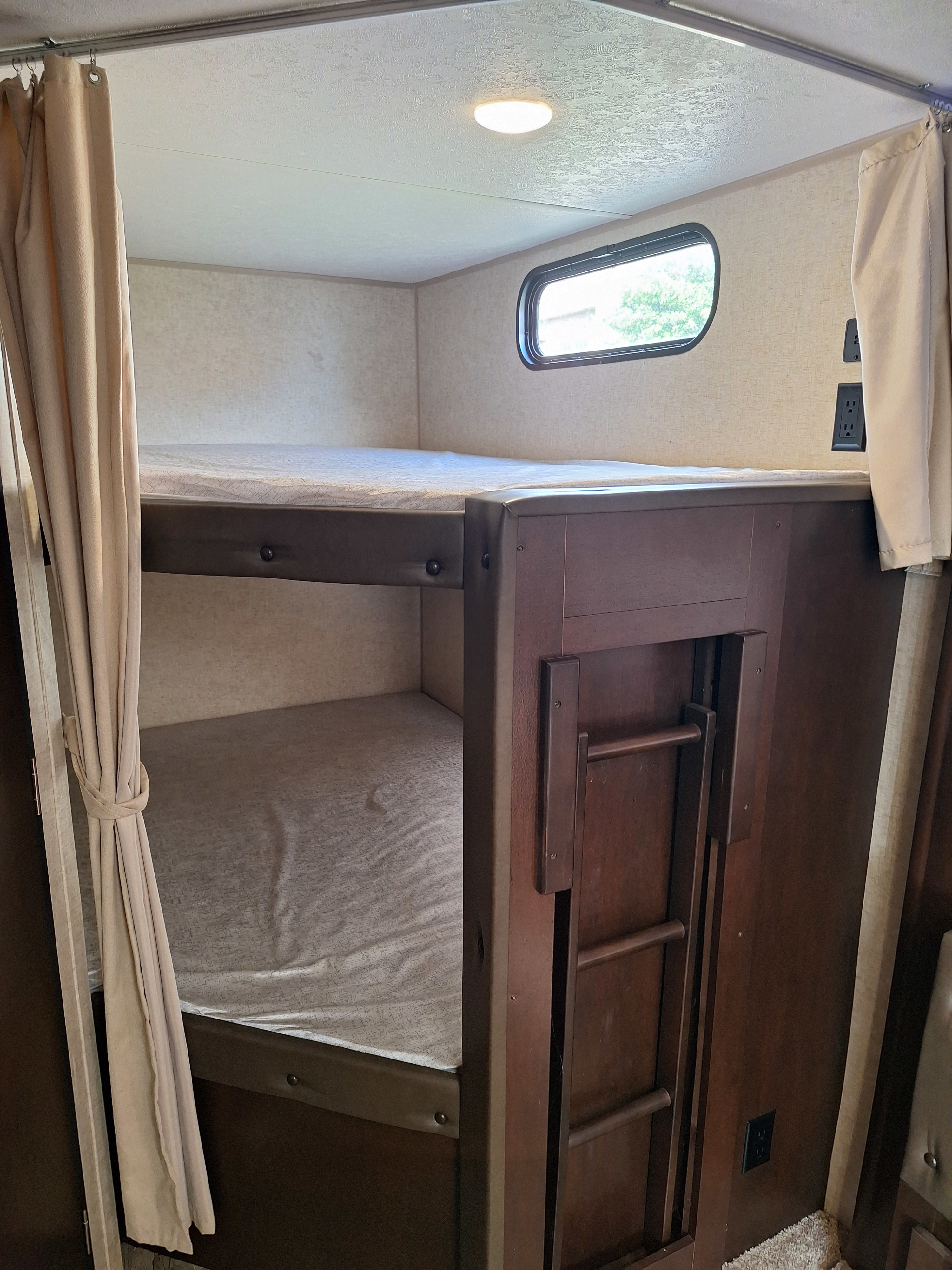 Inside an RV rental: two bunk beds with curtains, a window, and a light. A ladder provides access to the top bunk.. Forest River Cherokee 2018