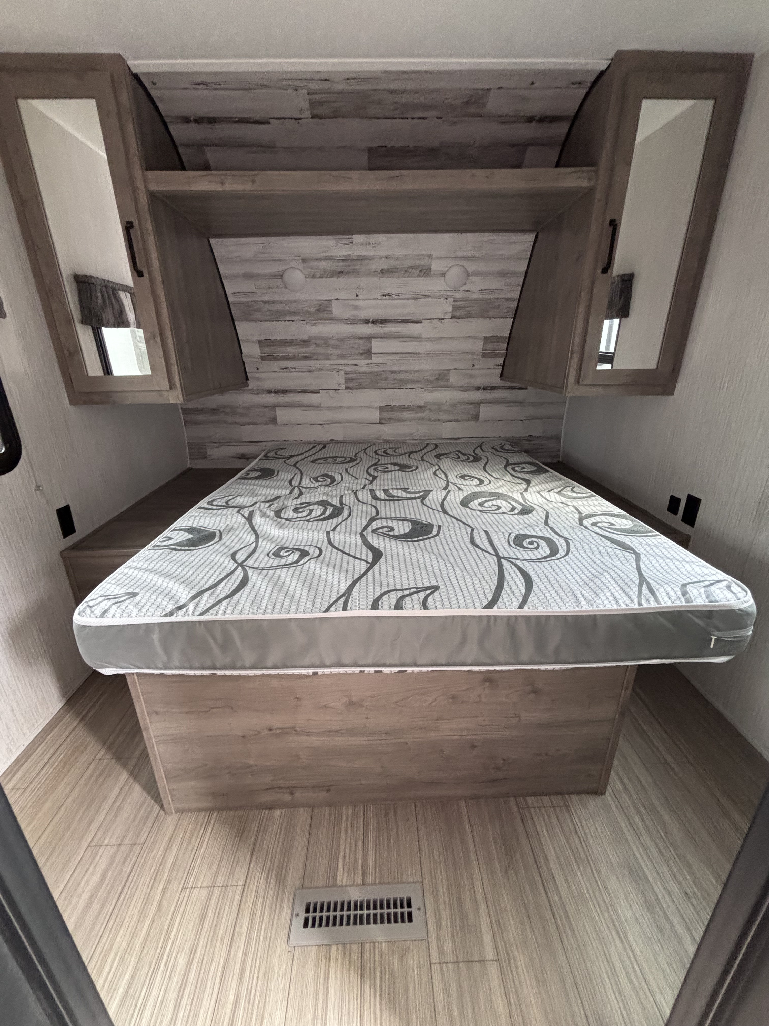 Comfortable RV rental bedroom with patterned mattress, overhead storage, wood finishes, and mirrored cabinets.. Palomino puma 2022