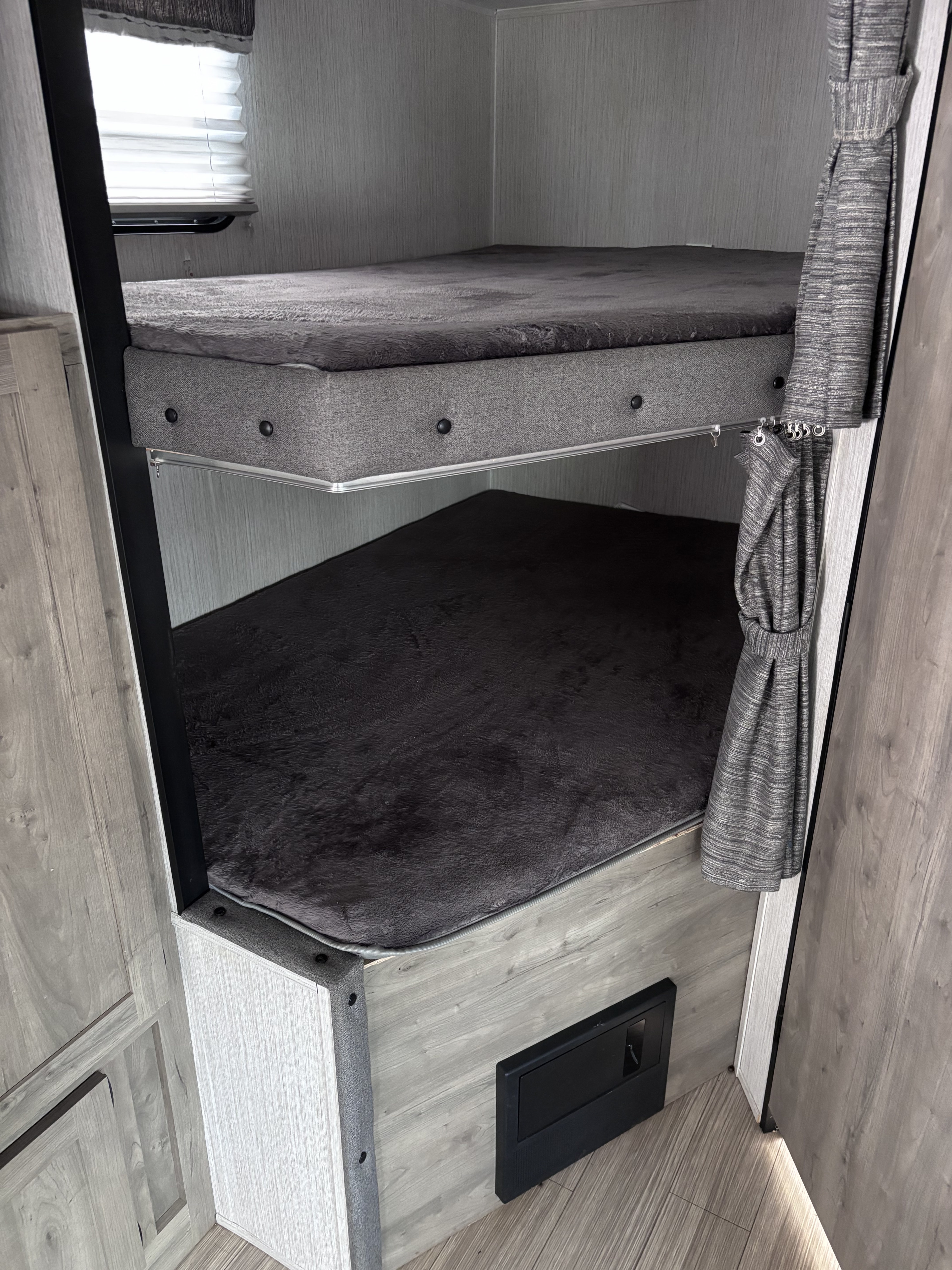 Interior of an rv rental featuring modern bunk beds with grey mattresses, privacy curtains, and a window, ideal for compact living.. Palomino puma 2022