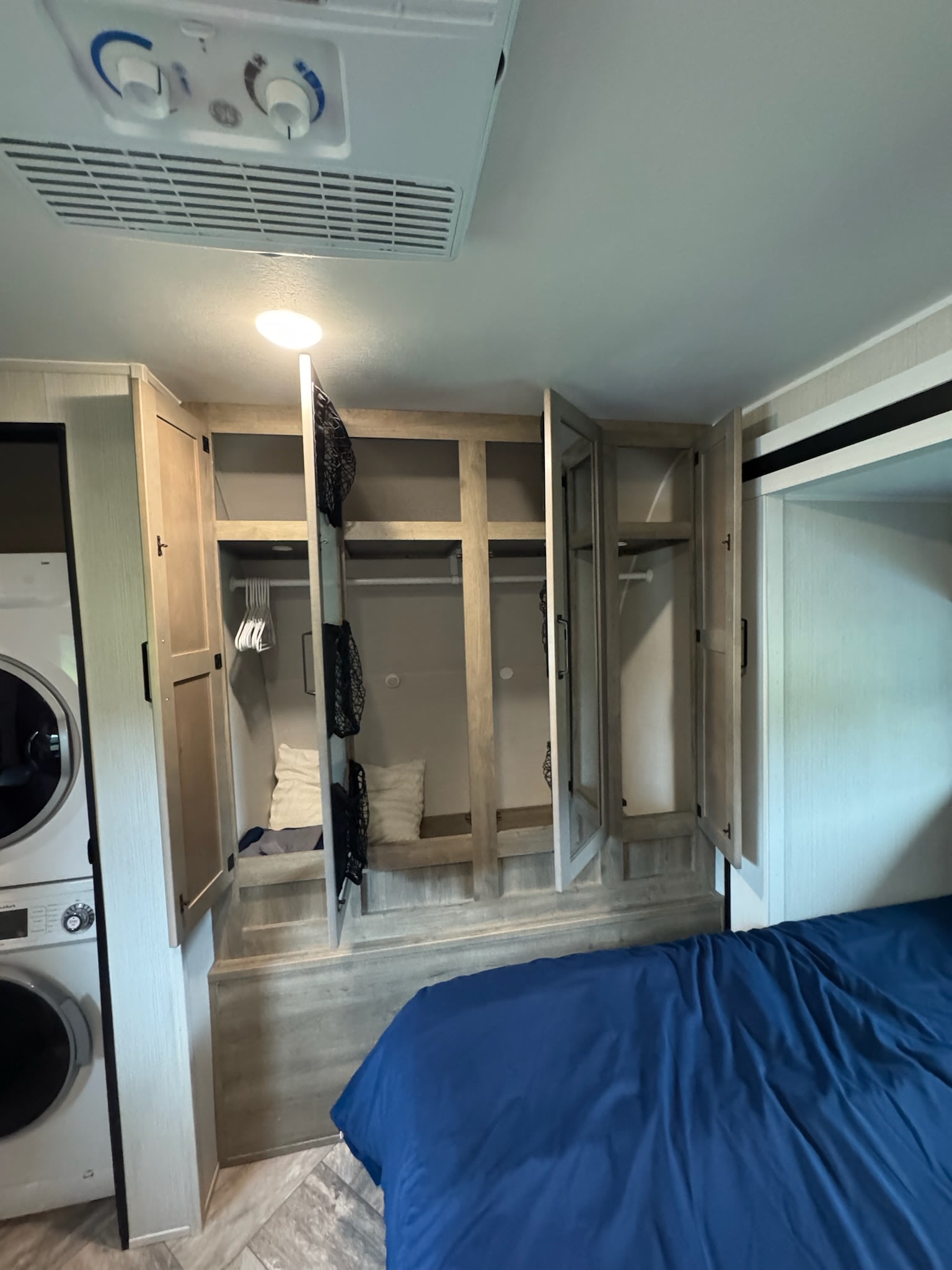 Explore this RV rental's bedroom: blue bed, smart built-in storage, stacked washer/dryer, and overhead AC unit.. Forest River Palomino Puma 2023