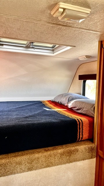 Cozy RV rental sleeping area features a bed with pillows, a striped blanket, and an overhead skylight for travel comfort.. toyota tundra 2010