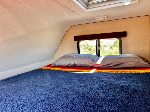 Relax in this bright RV rental bedroom. Features a comfy bed, pillows, colorful blanket, and a scenic window view.. toyota tundra 2010