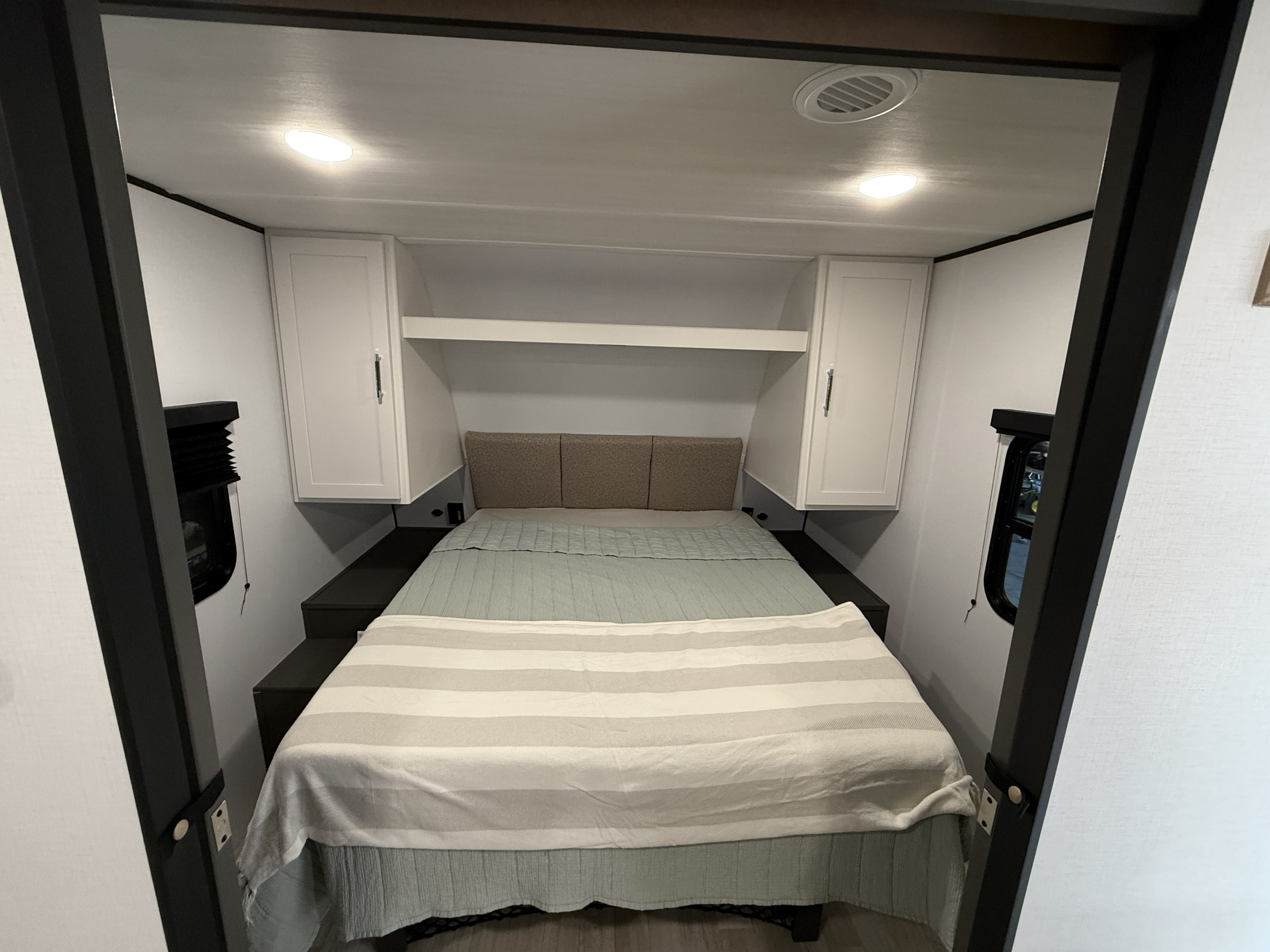 Inside a compact RV rental bedroom: a cozy bed with green bedding, overhead storage, and side windows for light.. Keystone RV Bullet 2026