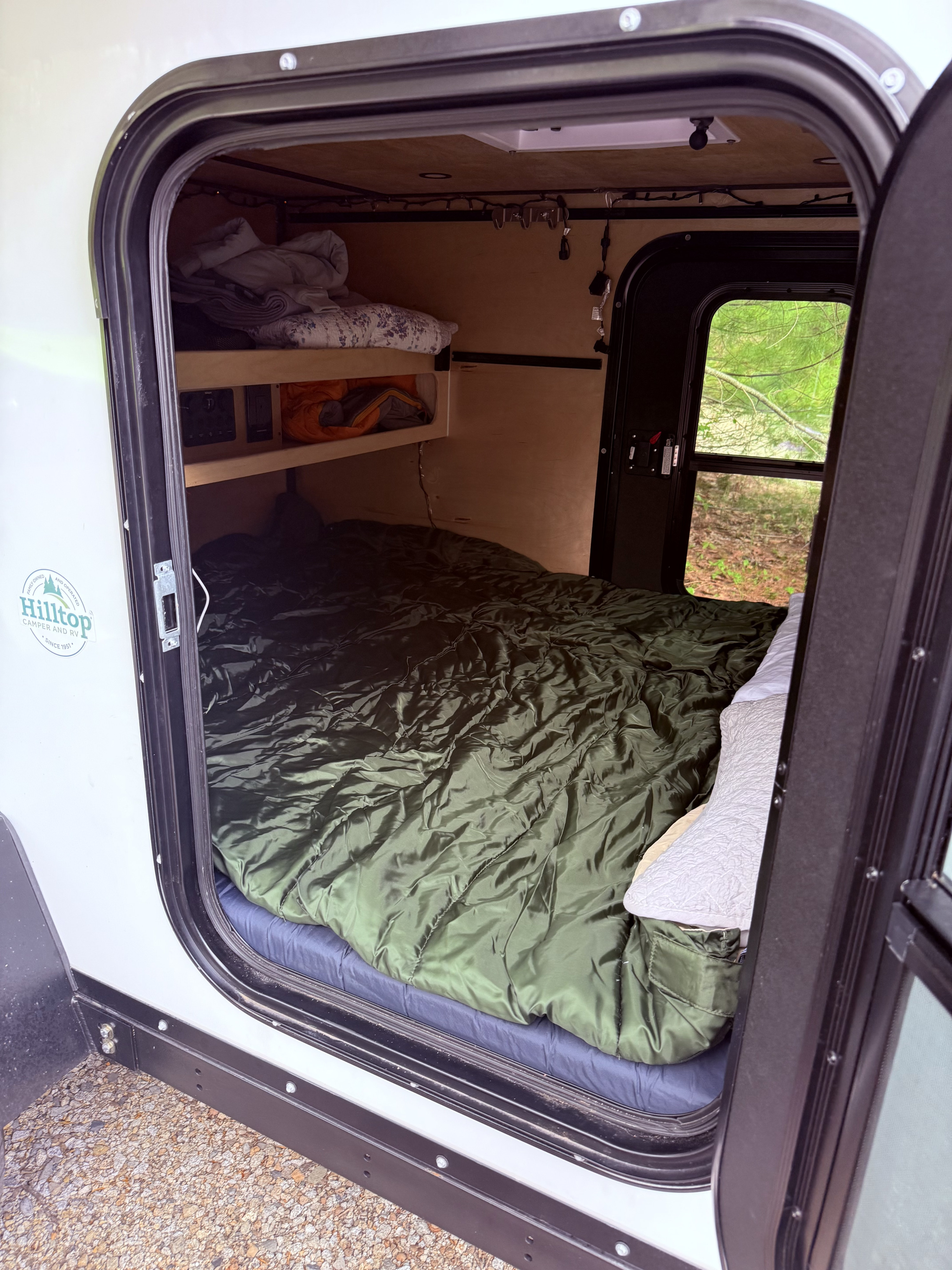 Cozy rv rental interior featuring a large bed, overhead shelves with bedding, and a window offering a view of nature.. Zion Off Road Z1 2025