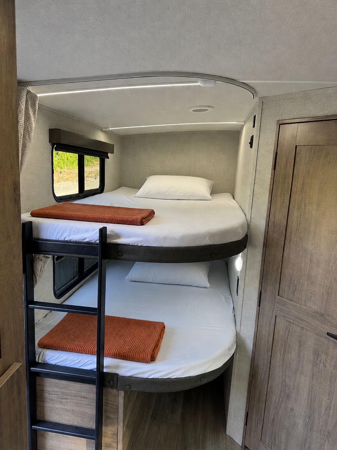 RV rental bunk beds feature crisp white linens, orange throws, window views, and integrated lighting for cozy nights.. Grand Design Imagine 2025