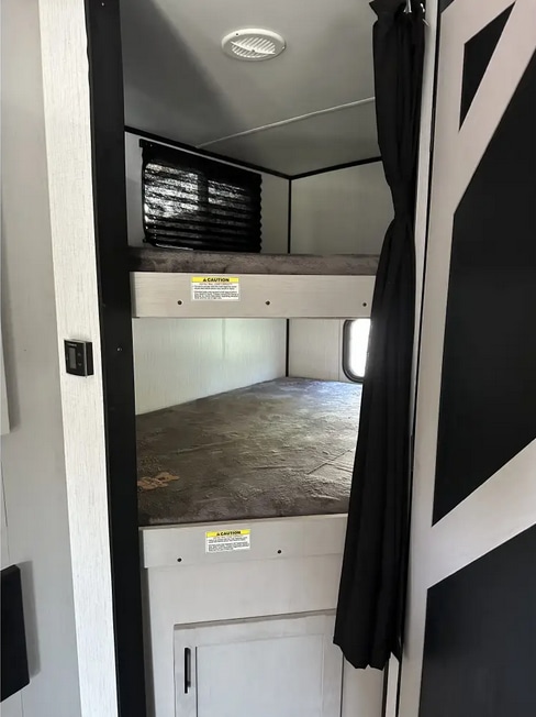 Interior view of an RV rental showing modern bunk beds, a ceiling vent, privacy curtain, and window for comfortable lodging.. Heartland RVs Mallard 2022