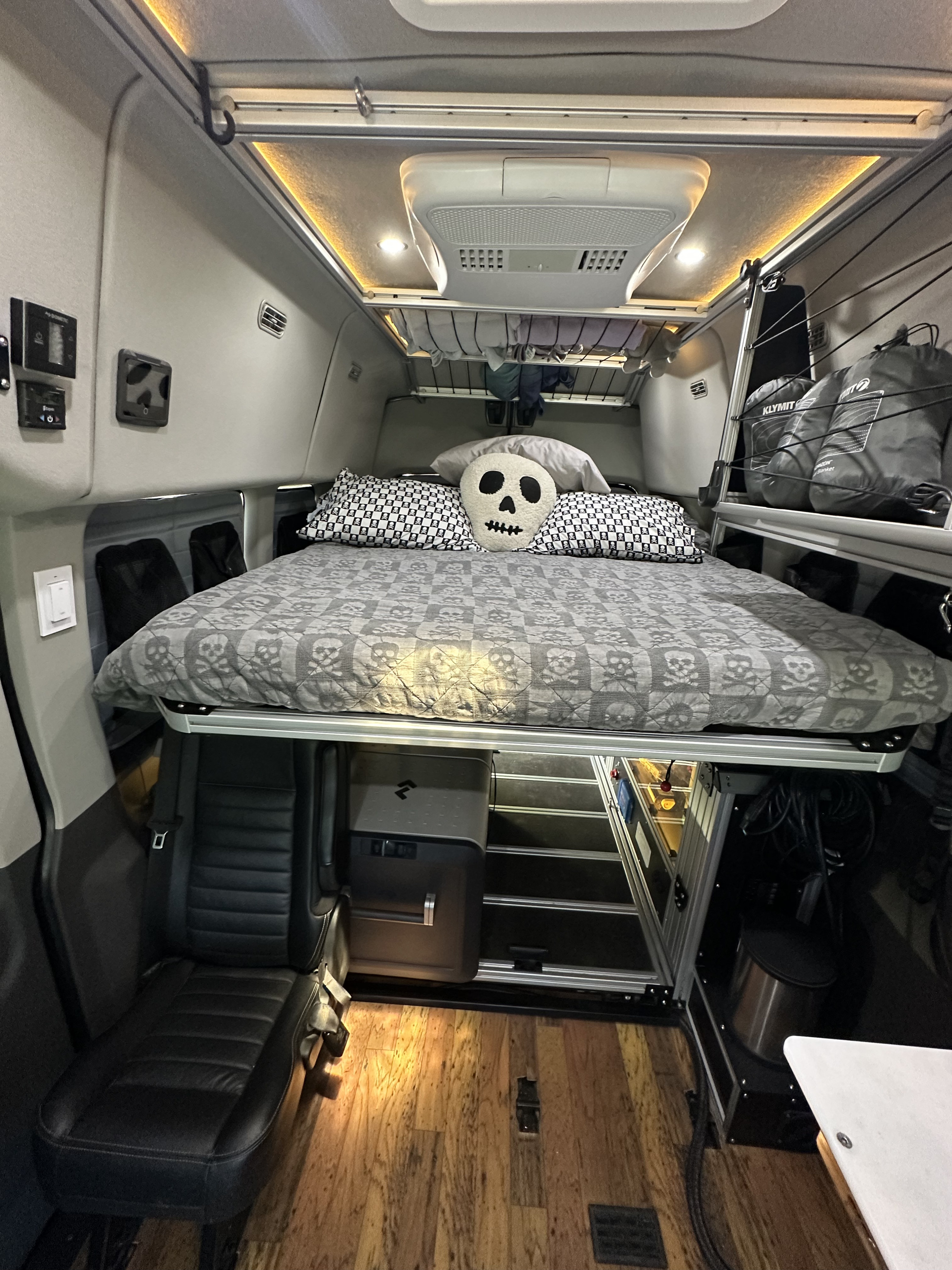 This modern rv rental camper van interior features a skull-themed raised bed, integrated fridge, seating, and overhead storage.. Ford Transit Custom 2021