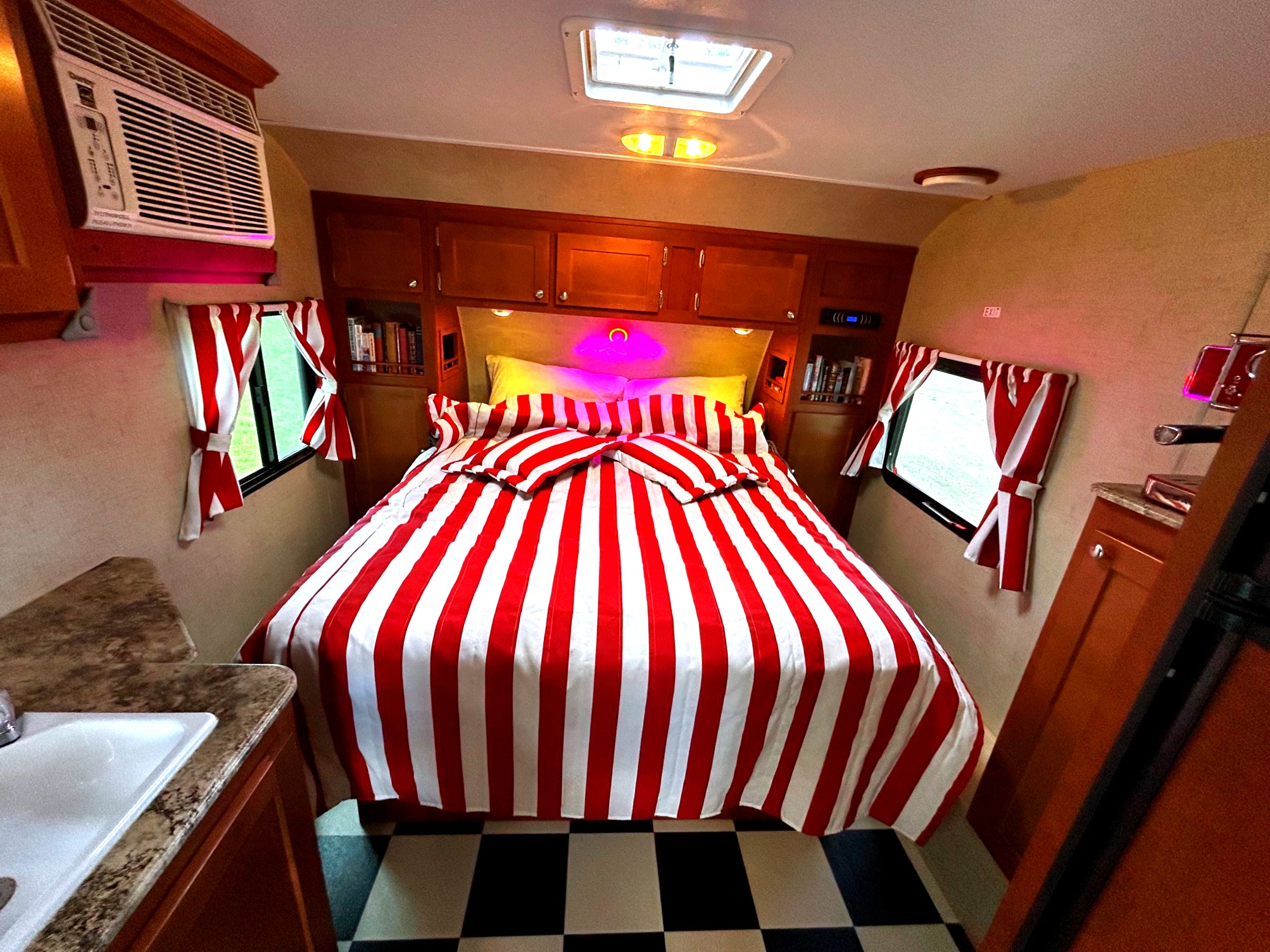 This vibrant rv rental bedroom boasts red & white striped bedding, a black & white checkered floor, built-in cabinets, and an AC unit.. Whitewater Retro 177 2015