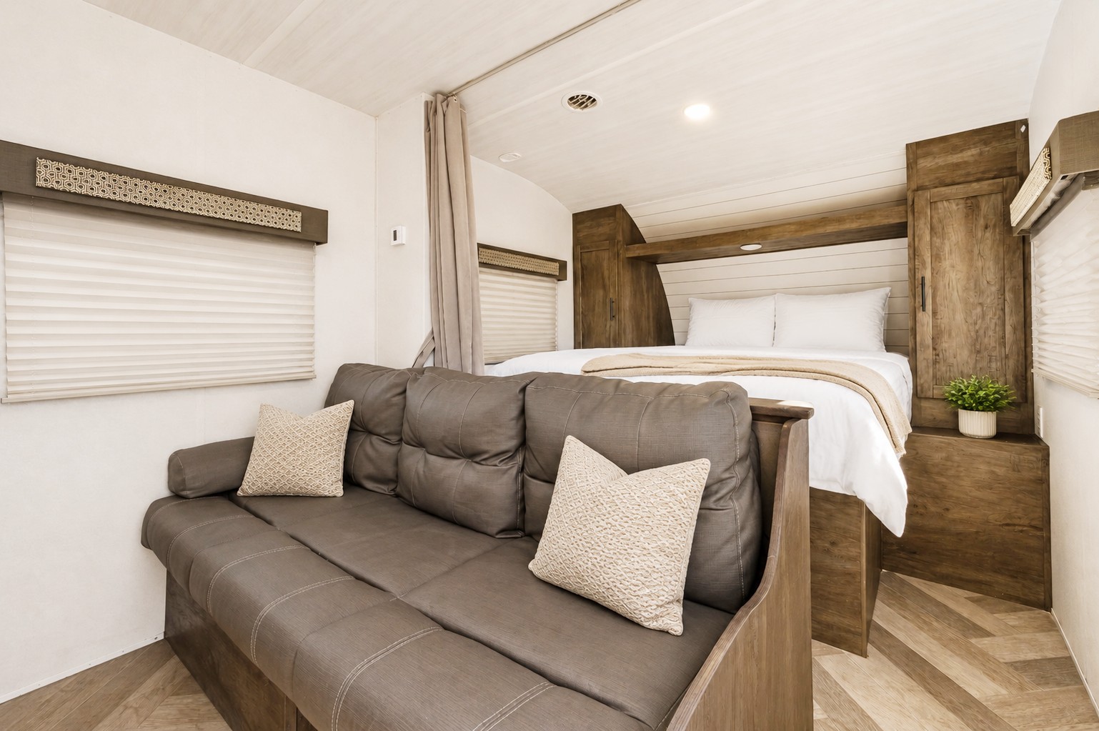 Cozy RV rental interior featuring a gray sofa with pillows and a comfortable bed with wooden accents. Ideal compact living space.. Forest River Wildwood X-Lite 2020