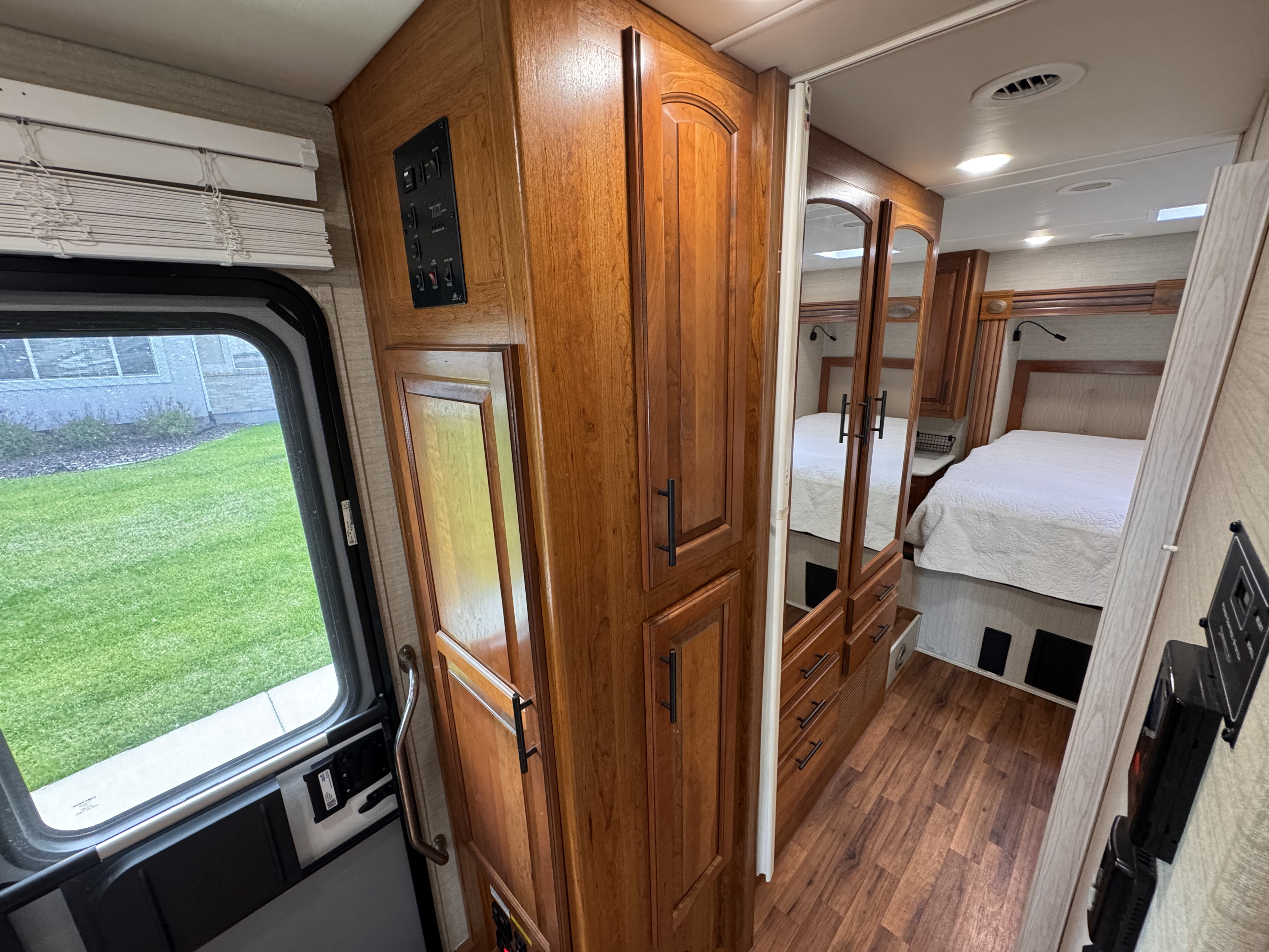 Bright rv rental interior highlighting a comfortable bedroom, wood cabinetry with controls, and a window overlooking green scenery.. Jayco Greyhawk 2017