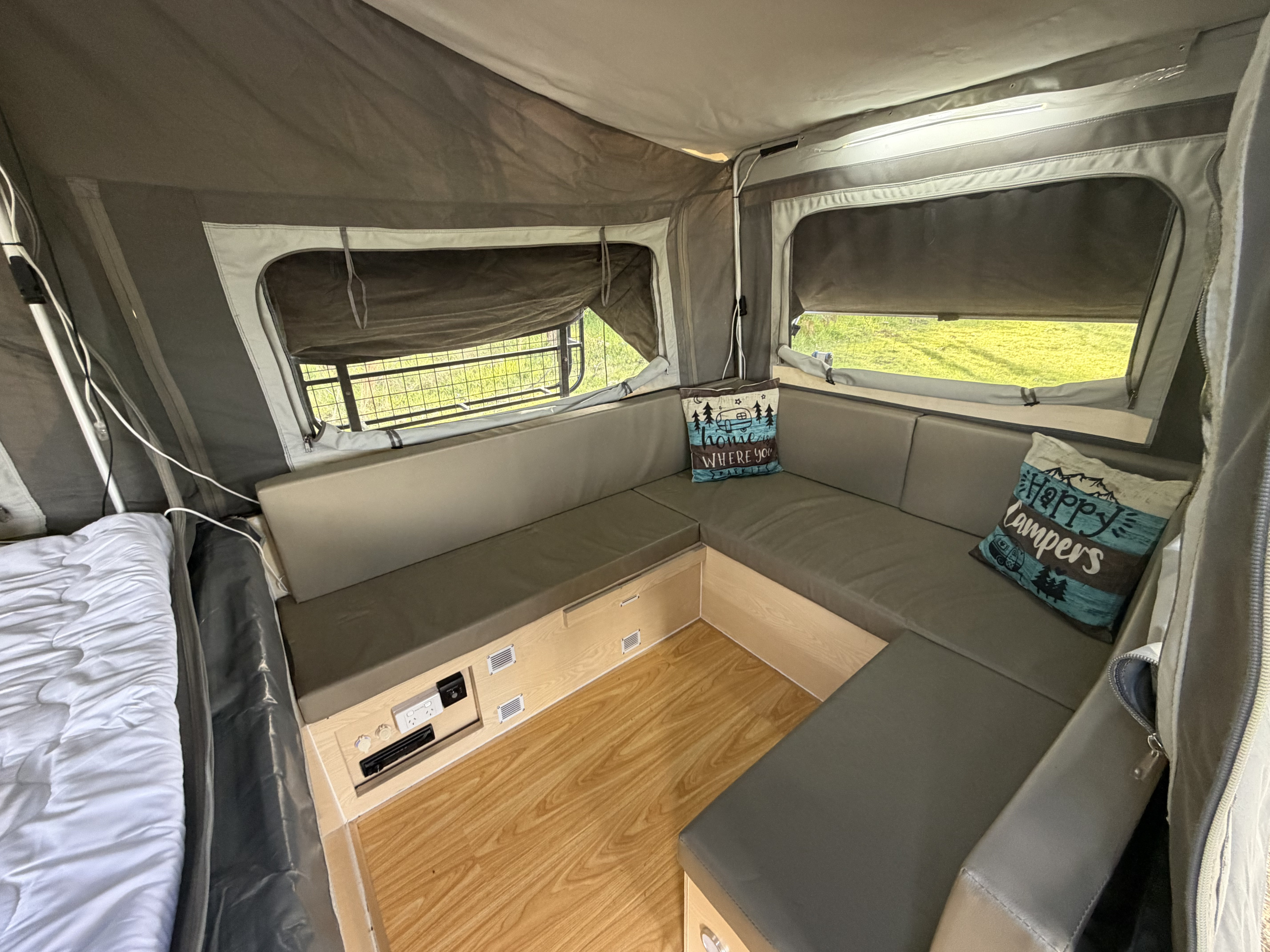 Interior of an RV rental: a comfy U-shaped bench, bed, wood-look floor, and screened windows. Ideal for camping.. EzyTrail Stirling GT MK 3 2022