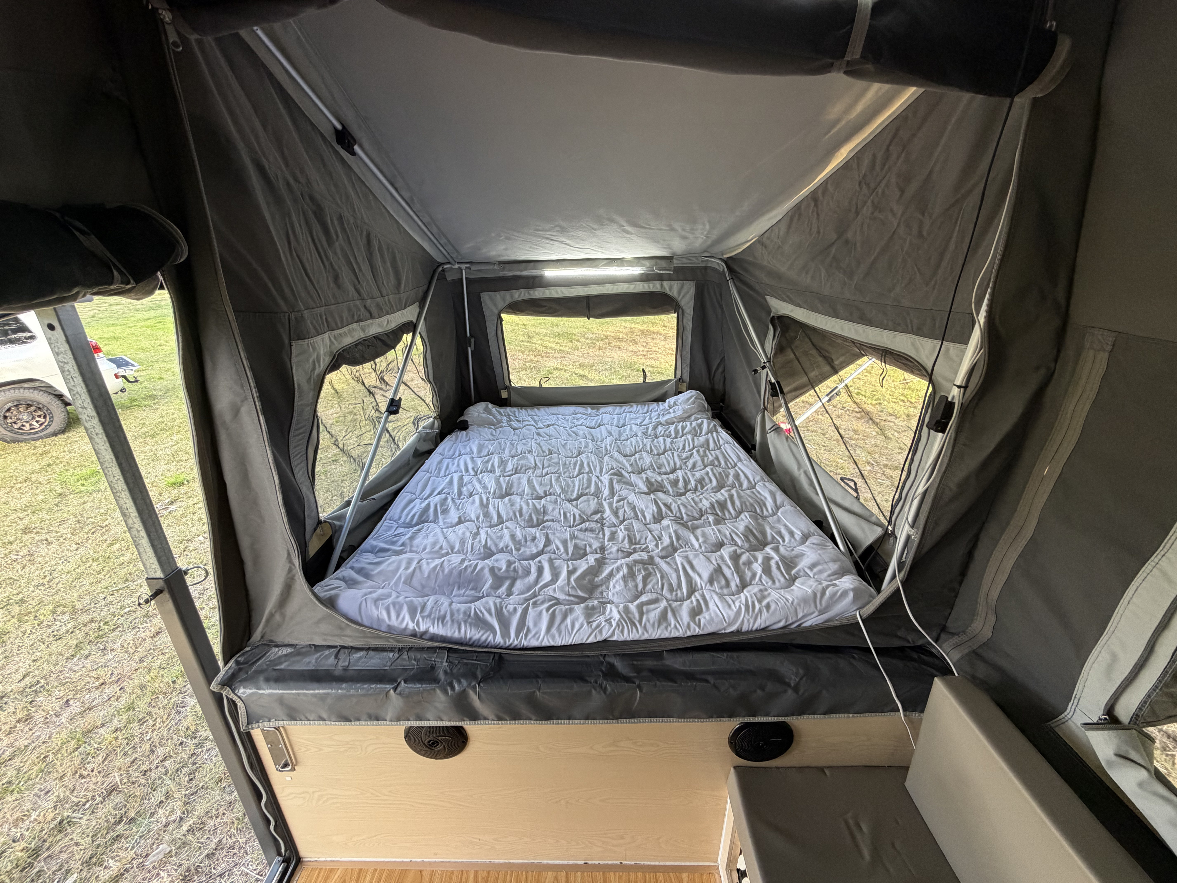 Cozy bed inside a pop-up RV rental, ready for adventure. Features windows, interior LED lighting, and lower storage/seating.. EzyTrail Stirling GT MK 3 2022
