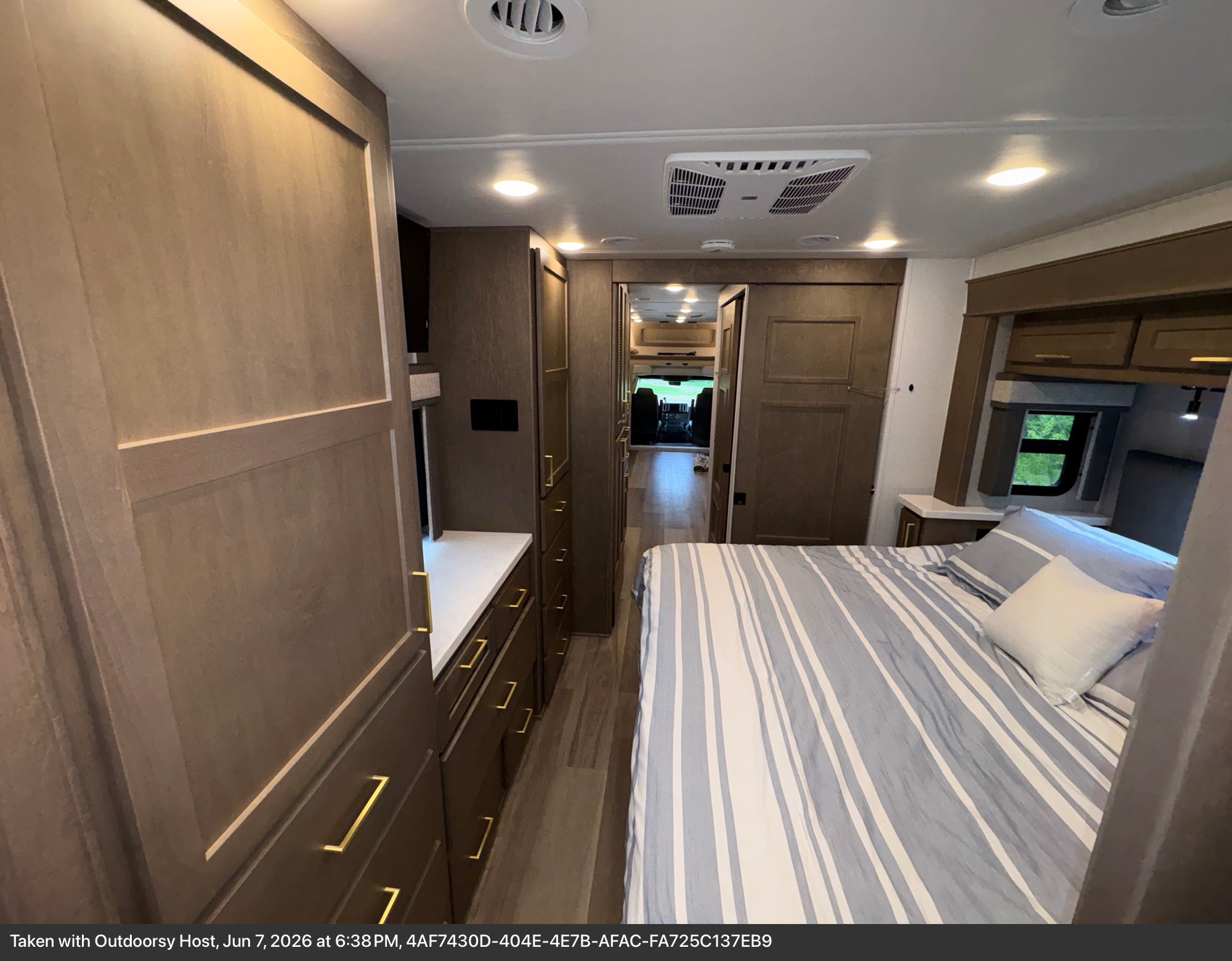 Modern RV rental bedroom: Features striped bedding, ample storage, and a bright hallway leading to the front.. Renegade Valencia 2026