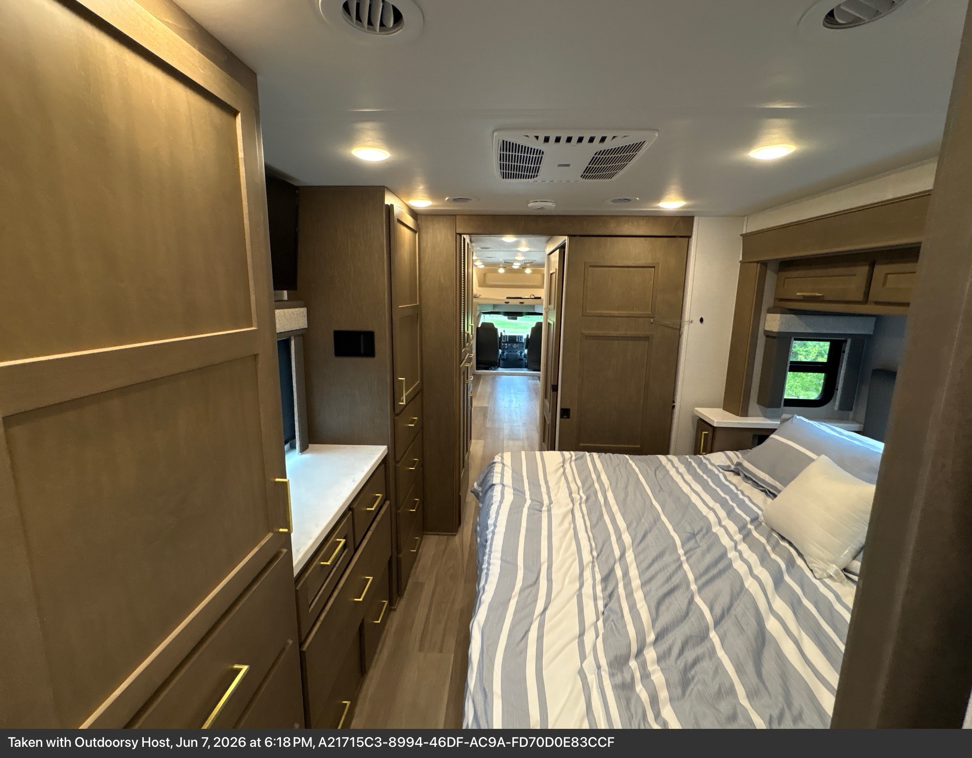 This RV rental offers a spacious interior with a comfortable bedroom featuring a blue and white striped bed, ample storage, and a view of the outside.. Renegade Valencia 2026