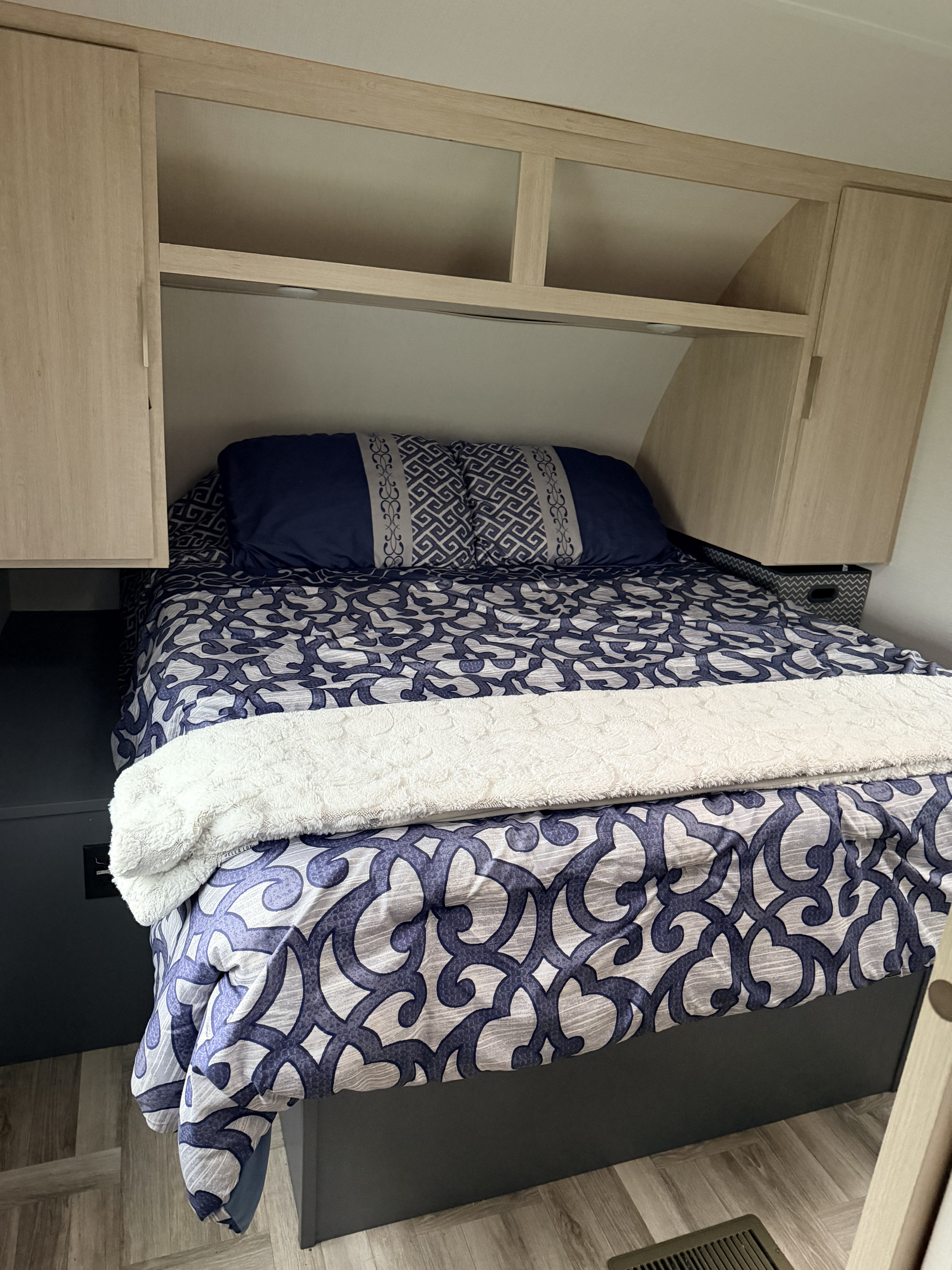 Cozy RV rental bedroom featuring patterned blue & white bedding, pillows, overhead cabinets, and built-in storage.. Forest River Tracer Ultra Lite 2025