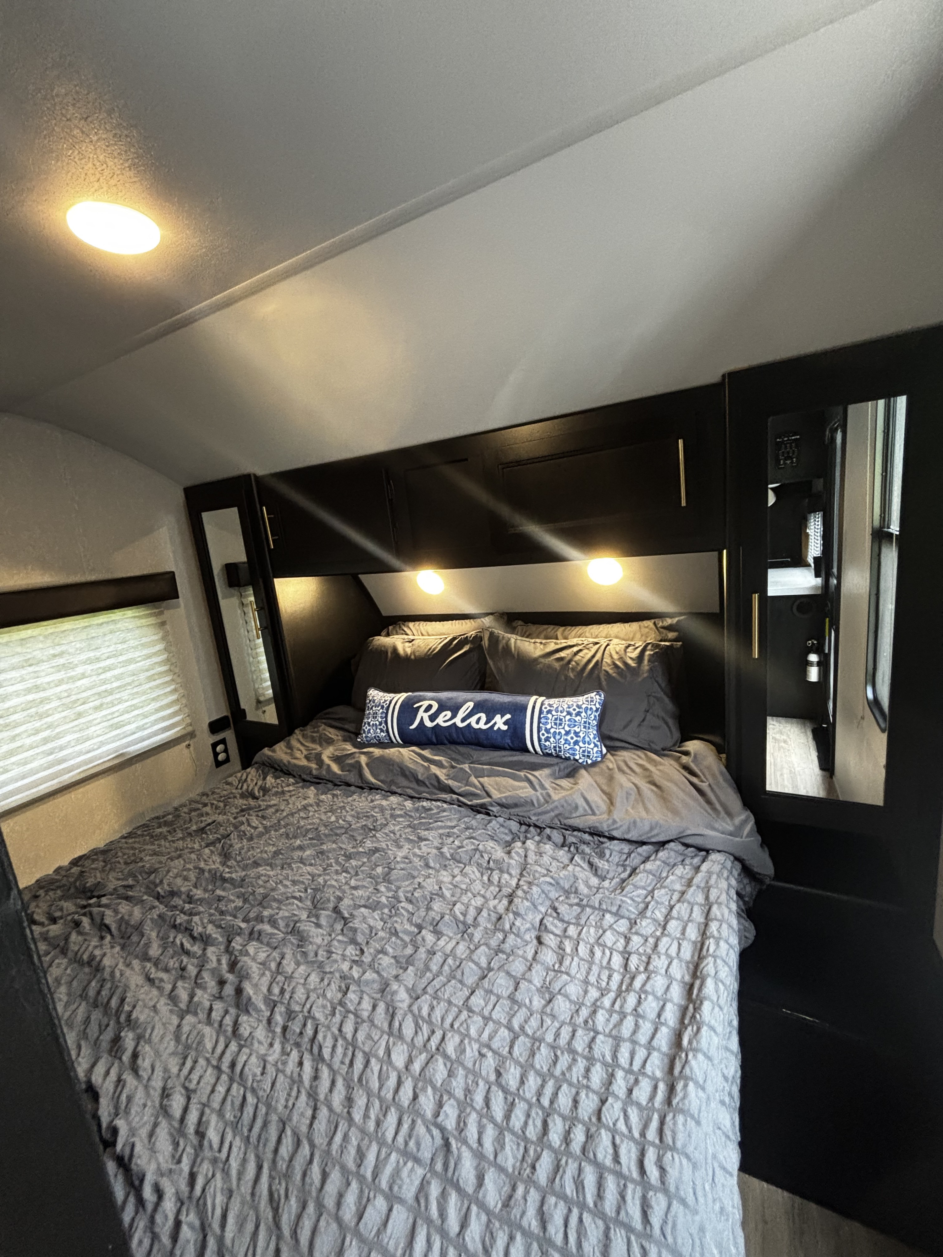 Cozy RV rental bedroom with a comfy bed, "Relax" pillow, and overhead storage, perfect for travel accommodations.. Forest River Cherokee Grey Wolf 2021
