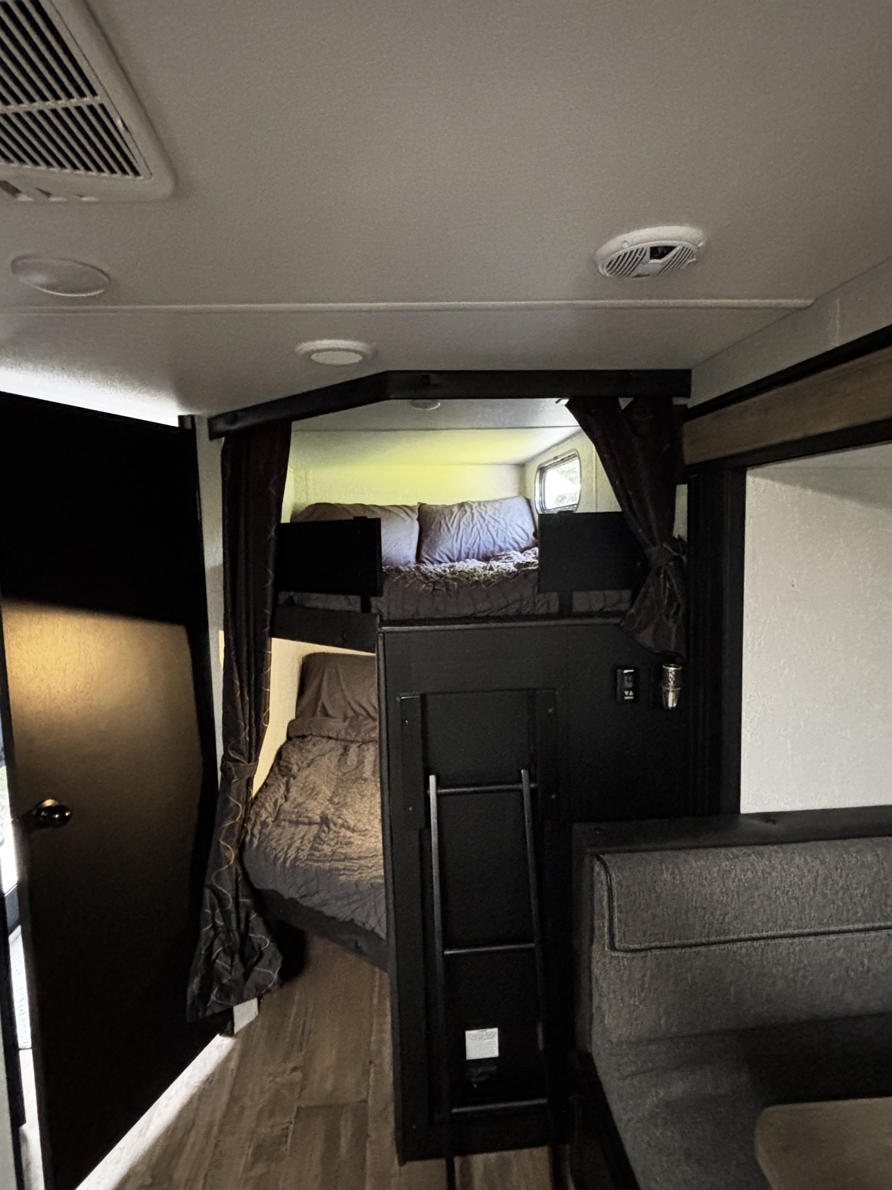 Cozy RV rental interior featuring bunk beds with a ladder on the left, a window above, and a dinette seating area on the right.. Forest River Cherokee Grey Wolf 2021