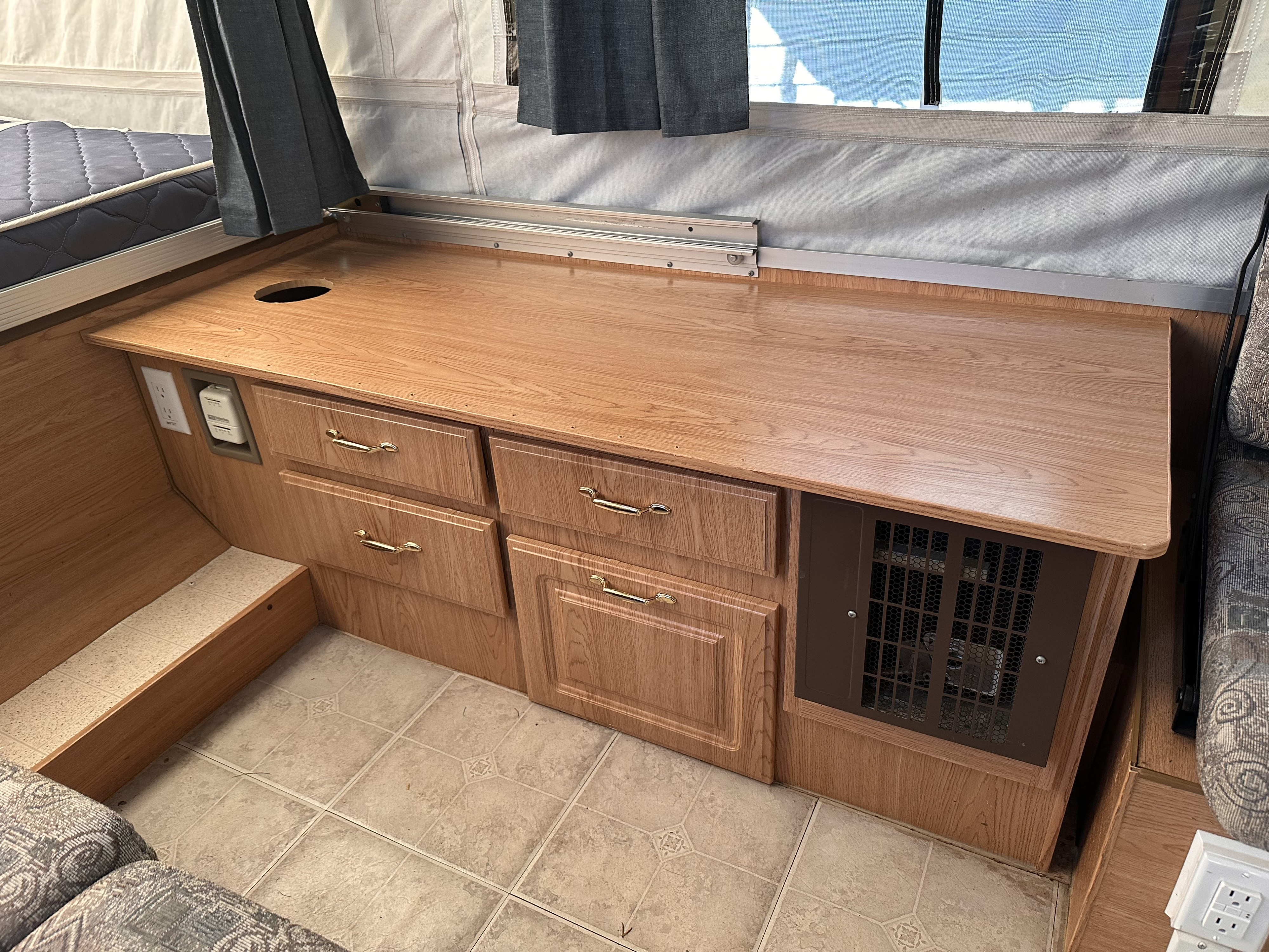 RV rental interior: wooden countertop, storage drawers, thermostat, outlet, and a pop-up bed area with canvas walls.. Forest River Rockwood Premier 2004