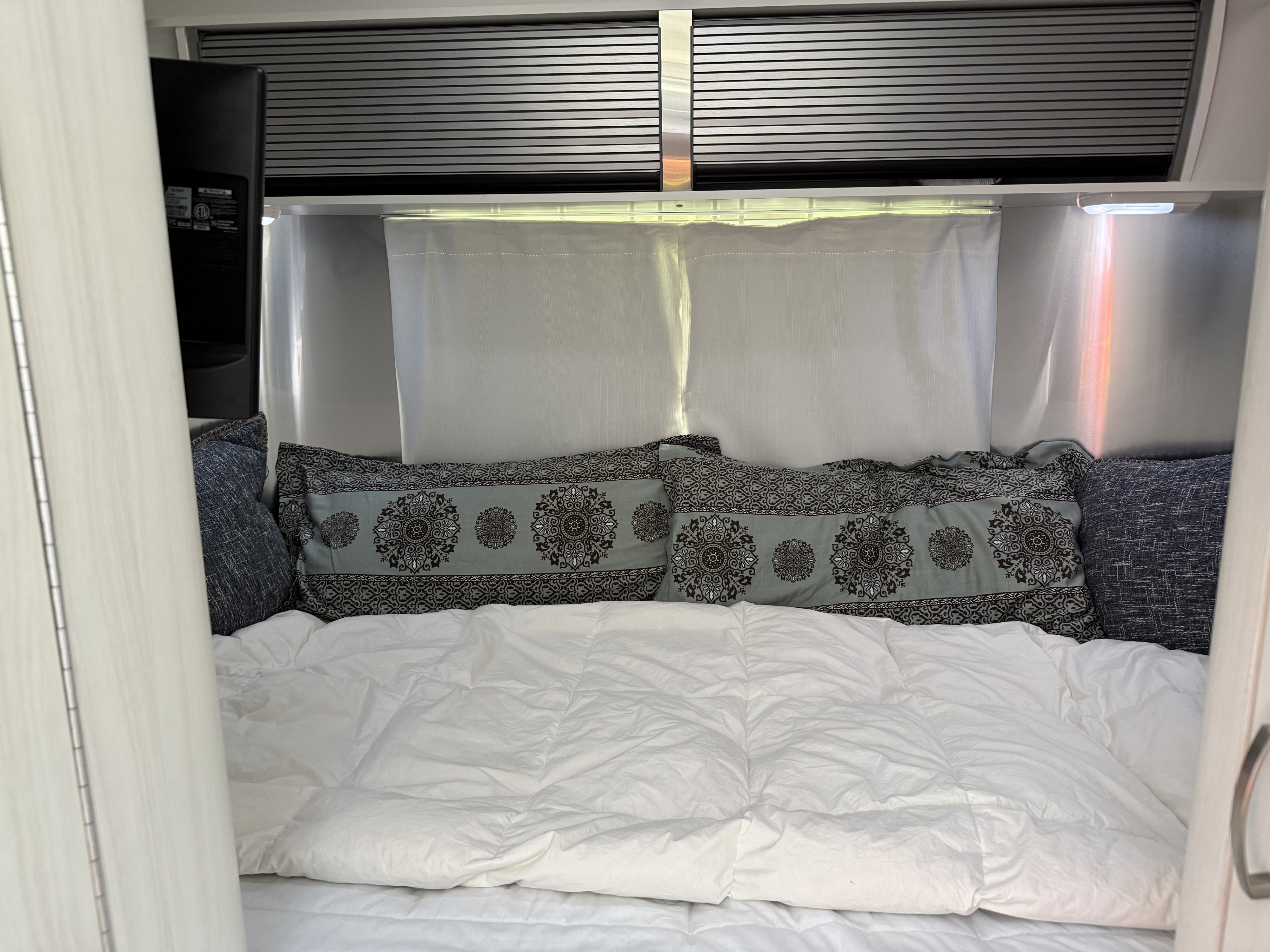 RV rental interior: a comfy bed with patterned pillows, white duvet, and modern overhead blinds/lighting.. Airstream Sport 2019