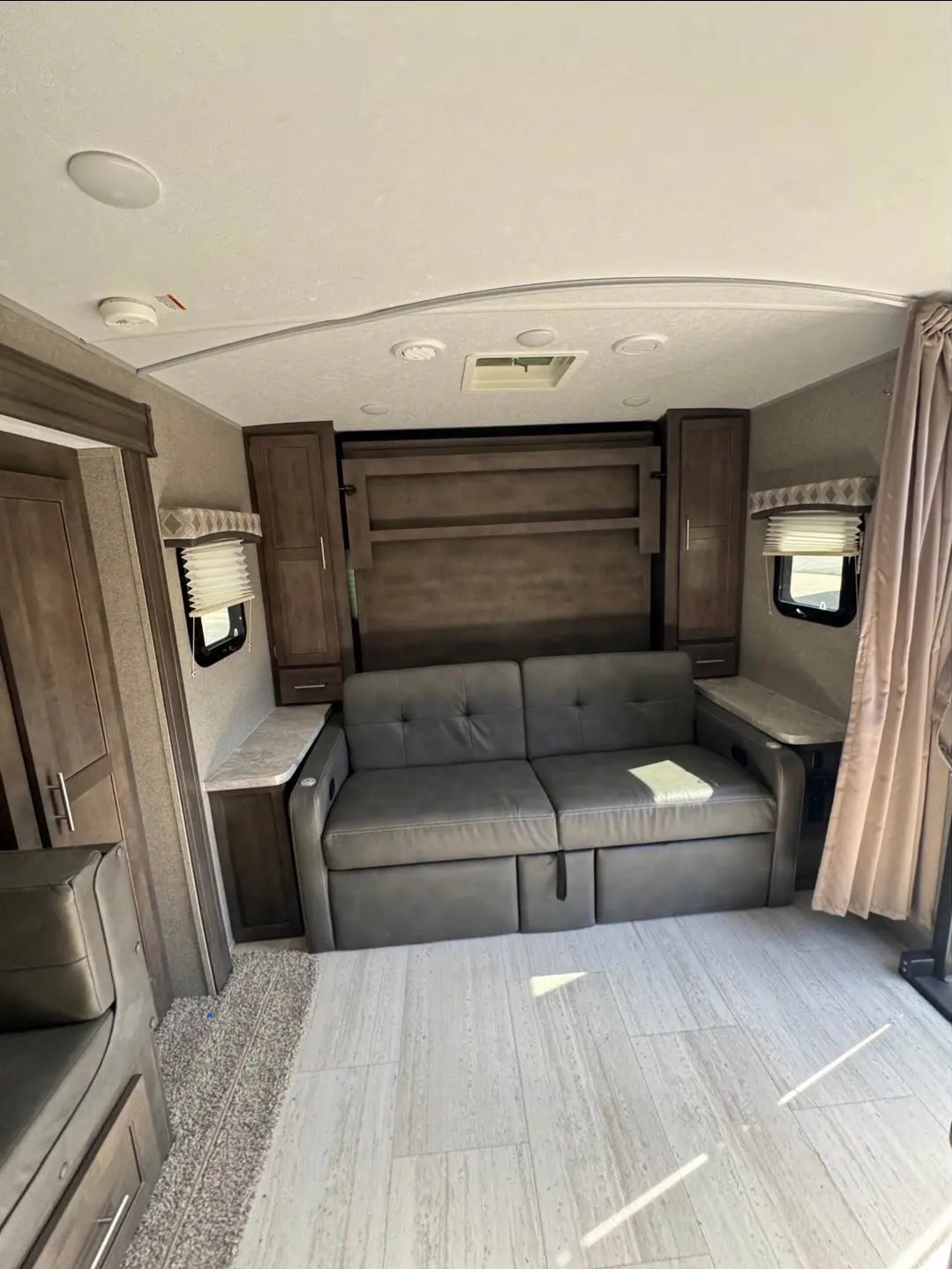 This rv rental's inviting living area features a comfy sofa, hidden murphy bed, and modern wood-look flooring.. Forest River Flagstaff Micro Lite 2020