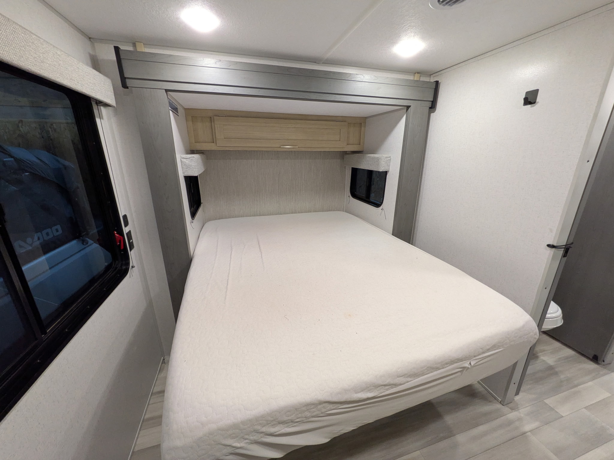 RV rental bedroom featuring a clean bed, overhead cabinet, and compact windows, ideal for travel and comfortable stays.. Forest River Wildwood FSX 2023