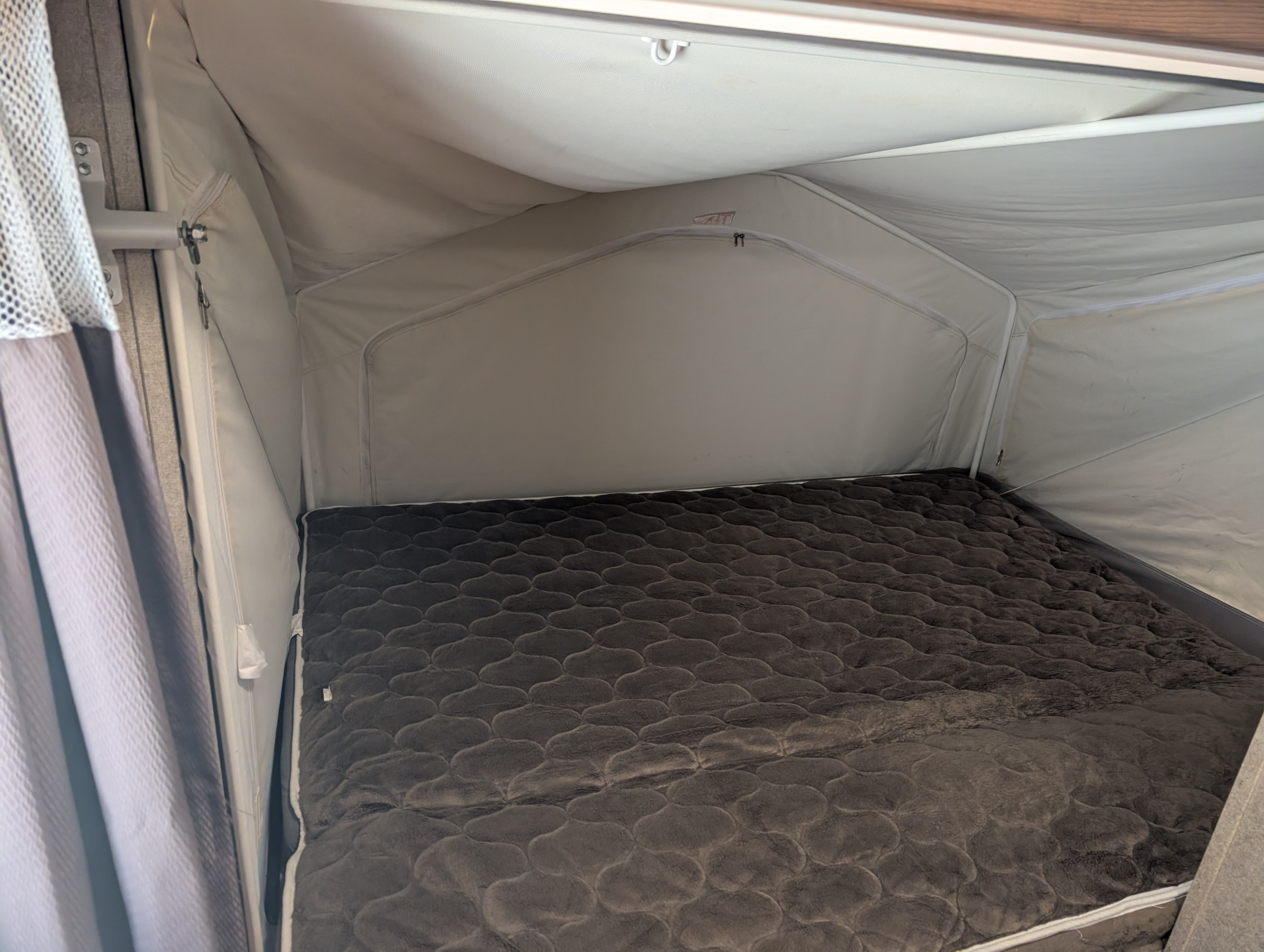 Cozy pop-up camper bed in an RV rental, featuring a gray textured comforter and canvas interior walls with light.. Forest River Rockwood Roo 2018
