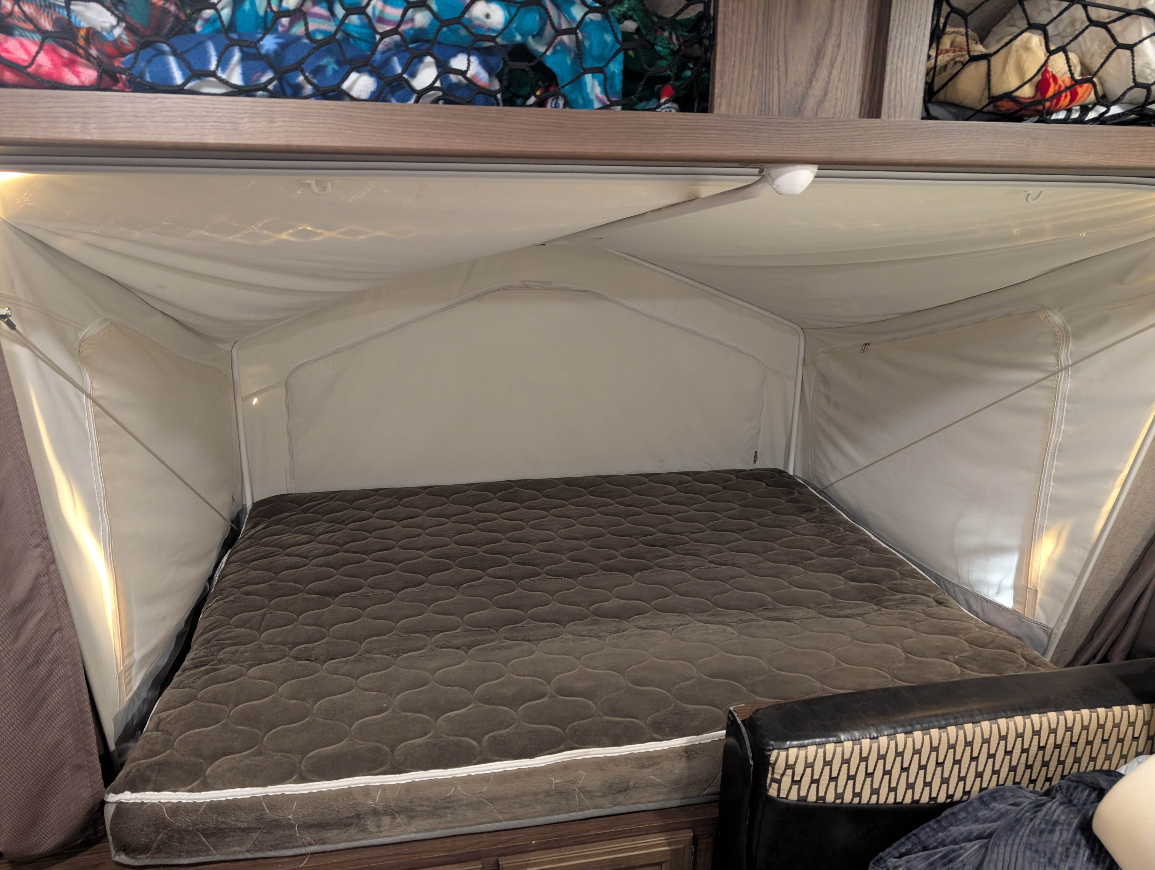 Cozy RV rental bedroom with a brown quilted mattress, canvas-like walls, and an overhead mesh storage net.. Forest River Rockwood Roo 2018