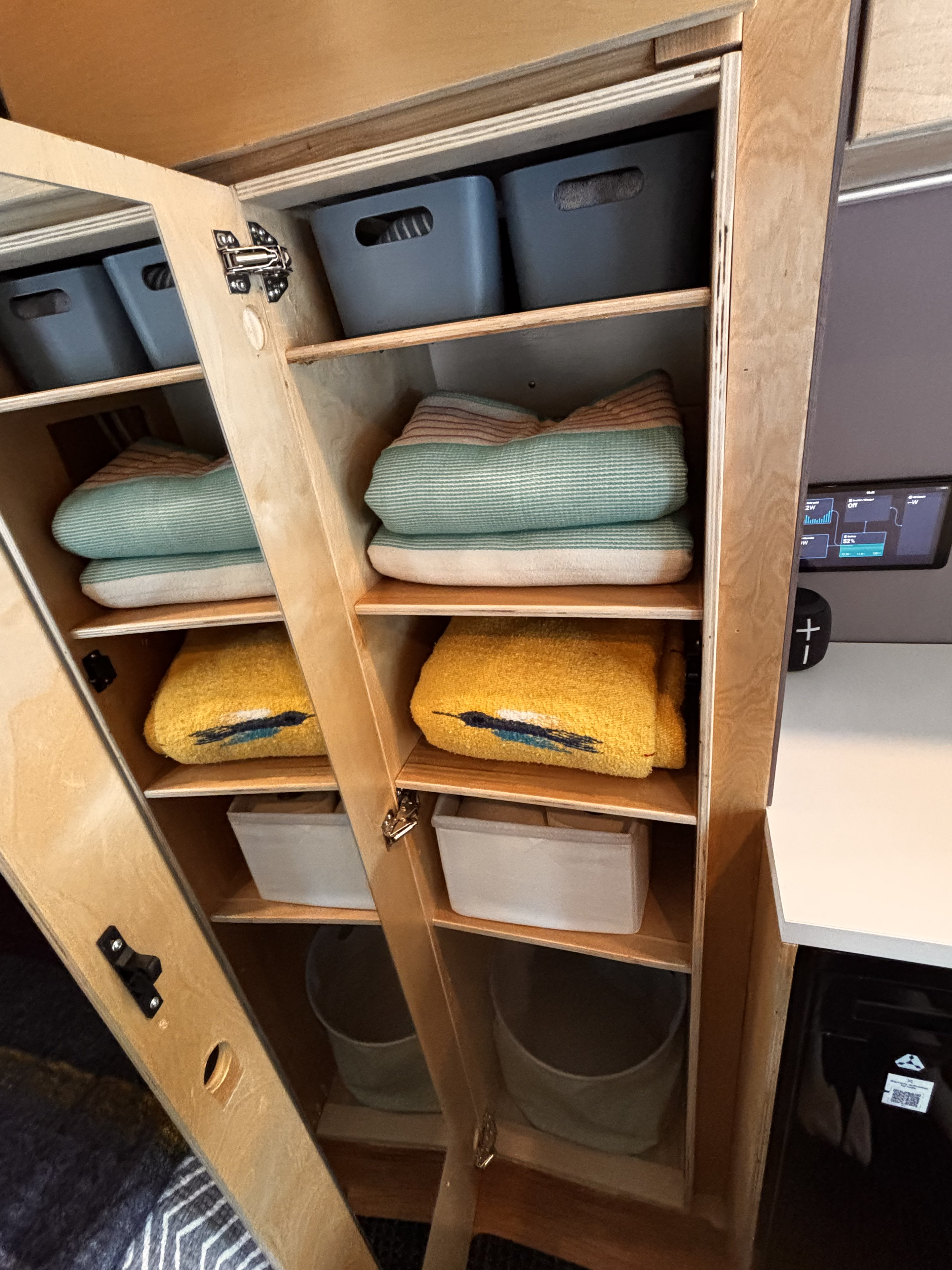 RV rental: Organized wooden cabinet storage with bins, striped blankets, and yellow towels. Compact living essentials.. Ford Transit 2021