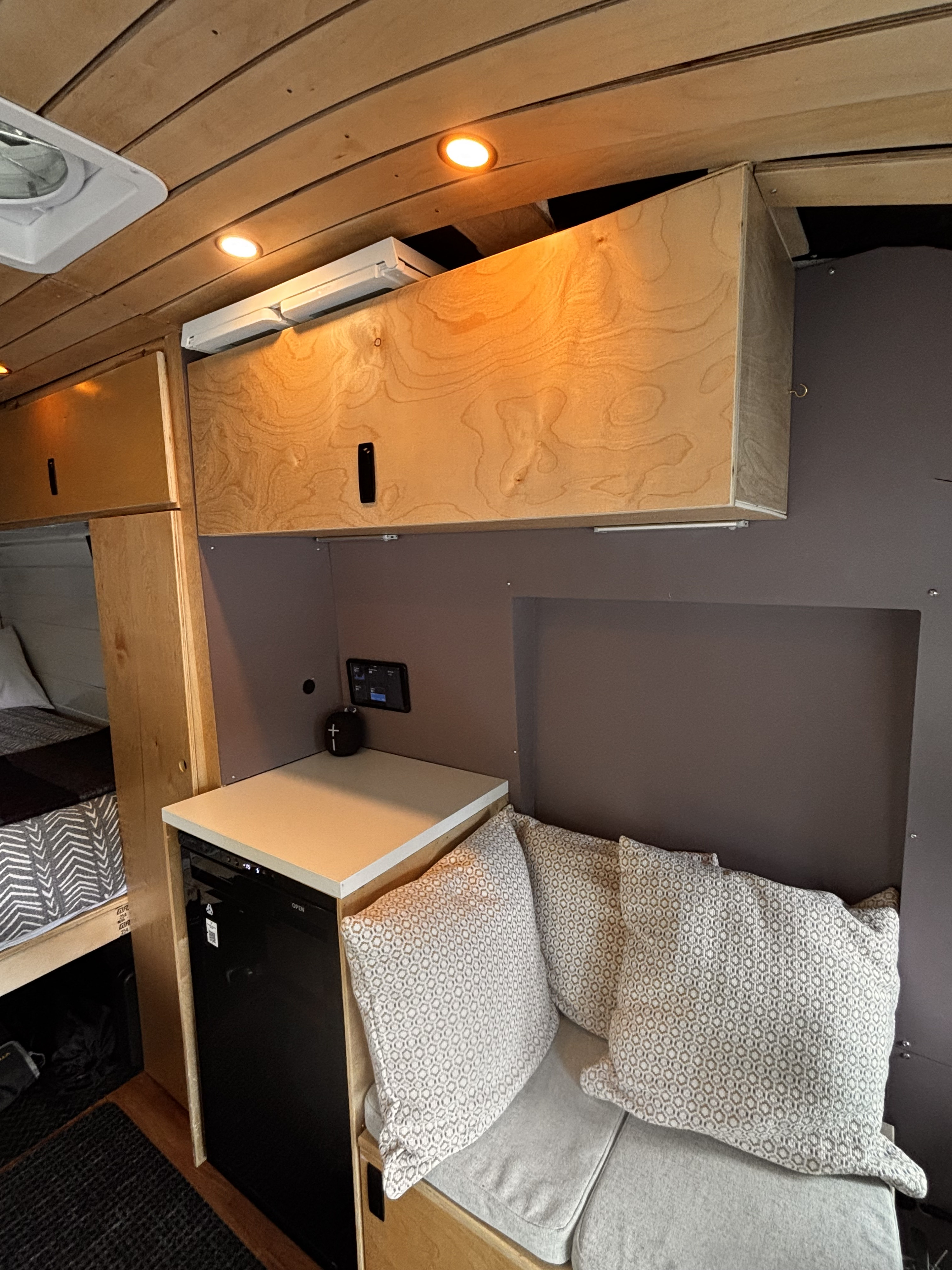 Cozy RV rental interior with wooden ceiling, overhead storage, a fridge, and comfy bench seating with pillows.. Ford Transit 2021